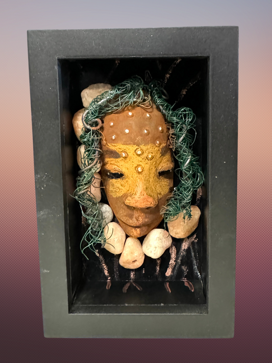 Monika is a "5x 7" raku mask displayed in a glass covered black shadowbox, accented with a beautiful two-tone honey brown complexion. Her intricate hair, made of 16 and 24 gauge wire, measures over 50 feet in length. With a contagious smile, Monika adds a touch of elegance to any home decor.