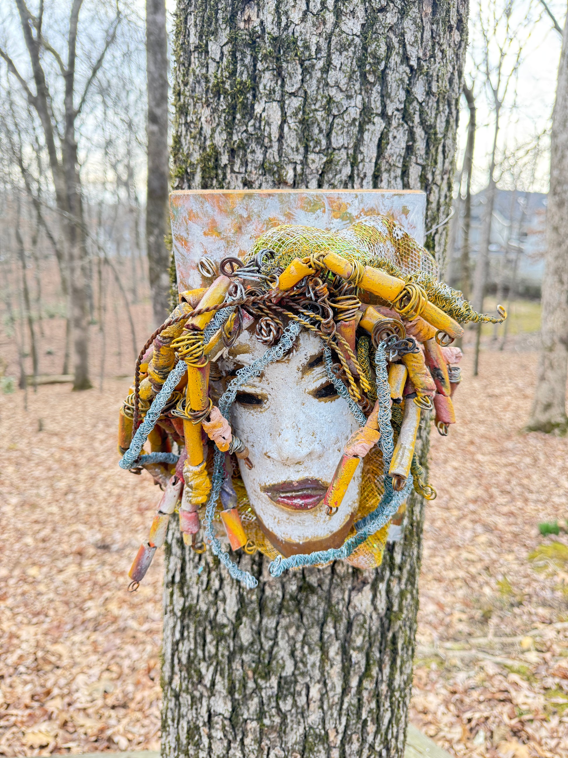 Experience the unique beauty of Amos, a mixed media raku fire mask carefully crafted with over 50 handmade beads and 50 feet of 24 and 16 gauge wire. Mounted on a 7” x 12” wood board and weighing approximately 4 pounds, Amos features an off-white face with braided and beaded &nbsp;hair. This one-of-a-kind masterpiece also includes several fabrics of netting in his hair, making it larger than most masks.