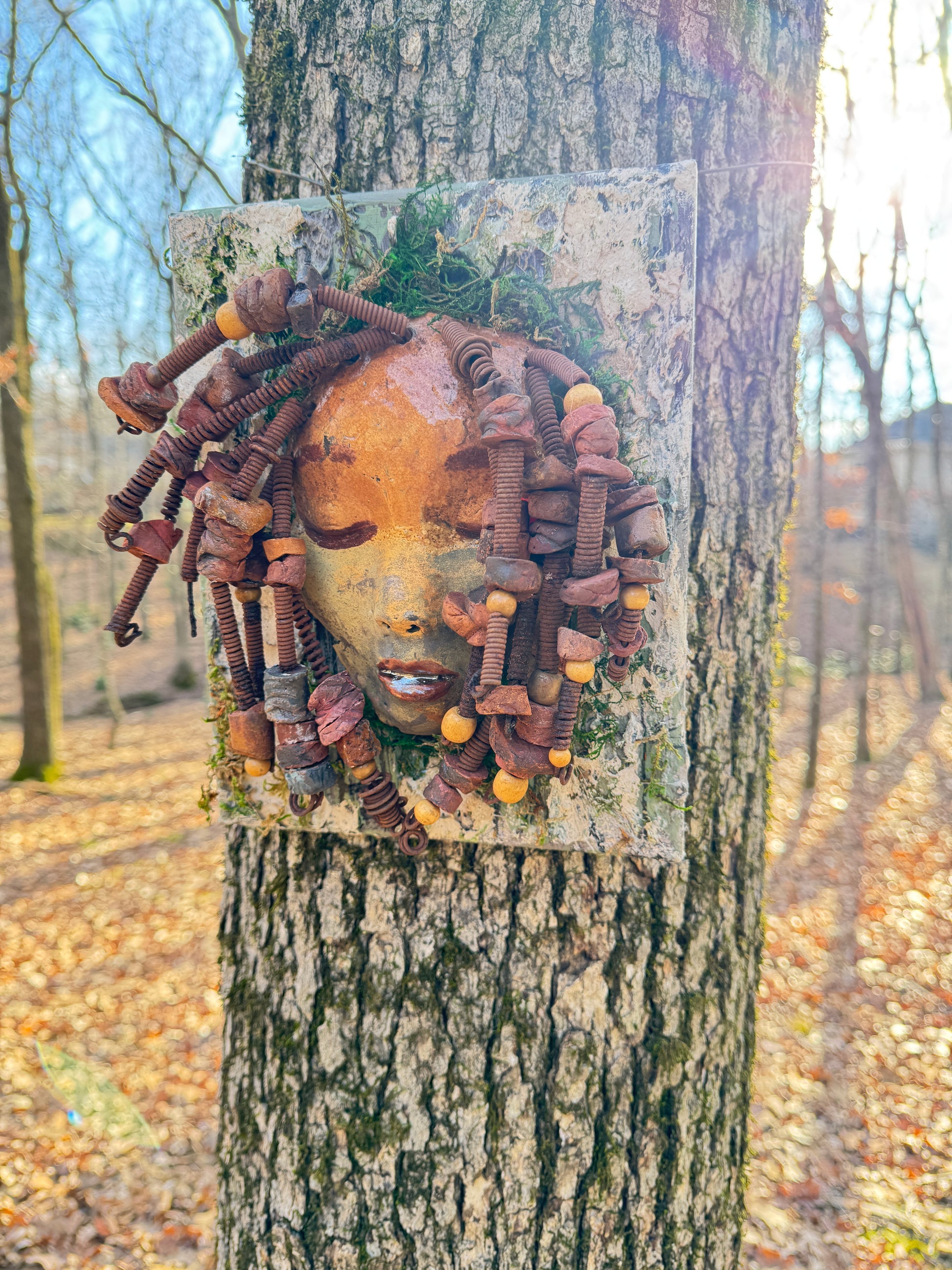 Discover the stunning aesthetic of EL Lay, a handmade raku fire mask adorned with 50 beads and crafted using 24 and 16 gauge wire. This one-of-a-kind piece weighs roughly 3 pounds and is mounted on an 8" x 10" canvas. The earthy two tone face and braided, beaded hair make it a unique addition to your indoor or outdoor decor.