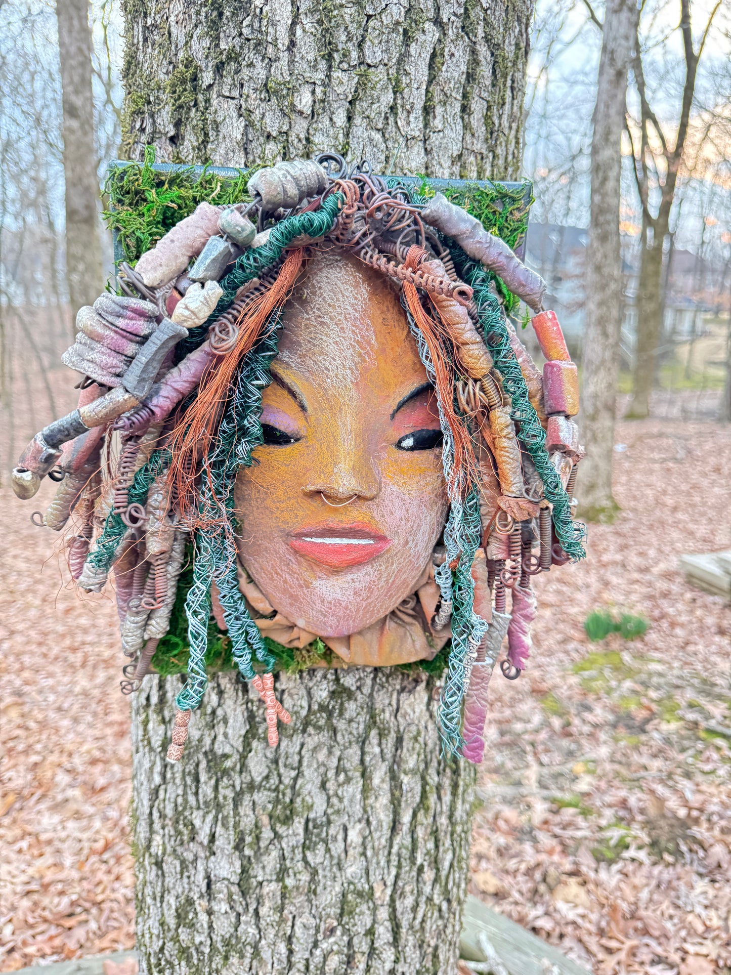 Uncover the magnificent charm of Dallas, a handcrafted raku fire mask embellished with over 60 beads and made using 24, 16 gauge wire and various mixed media. This exceptional creation has a weight of approximately 3 pounds and is attached to a 10” x 12" canvas. The natural two tone face and braided, beaded hair make it a distinctive addition to your indoor or outdoor design.