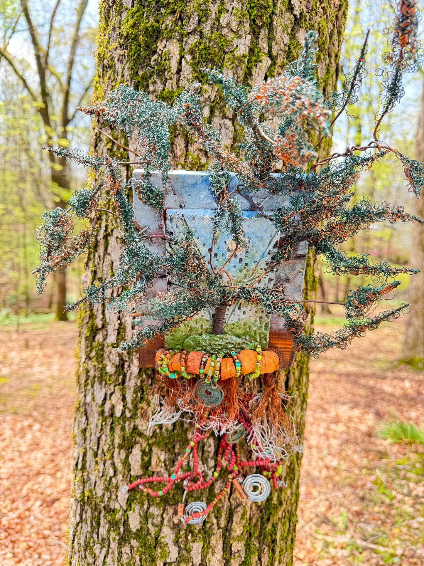 Discover the stunning Copper Cluster, measuring 18x15 inches, which blends 16- and 24-gauge wire with beautifully crafted Raku fire beads. As an added touch, a RAKU-fired hand-painted texture tile is mounted on a 8x7 wooden base. The sunlight streams through the lush copper foliage, evoking the feel of a refreshing spring day.