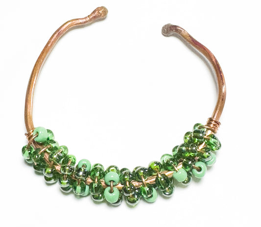 This copper-banded bracelet displays an alternating pattern of dark and light green beads, creating a sophisticated look for any ensemble.