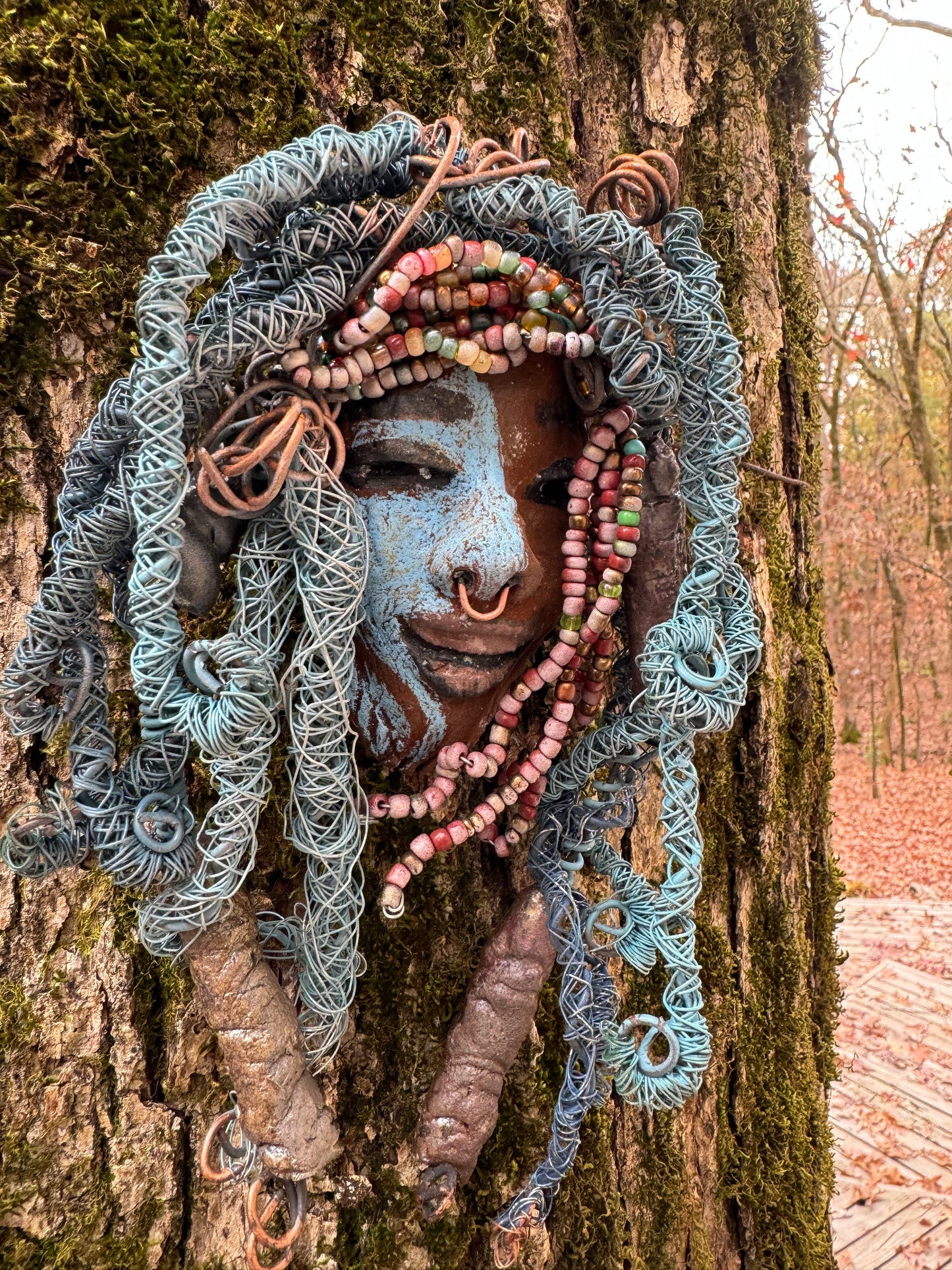 Zola is a mesmerizing raku mask with a captivating tribal face. She measures approximately 5 x 9" and weighs 7 oz. The mask is further decorated with blue hair and a copper nose ring.