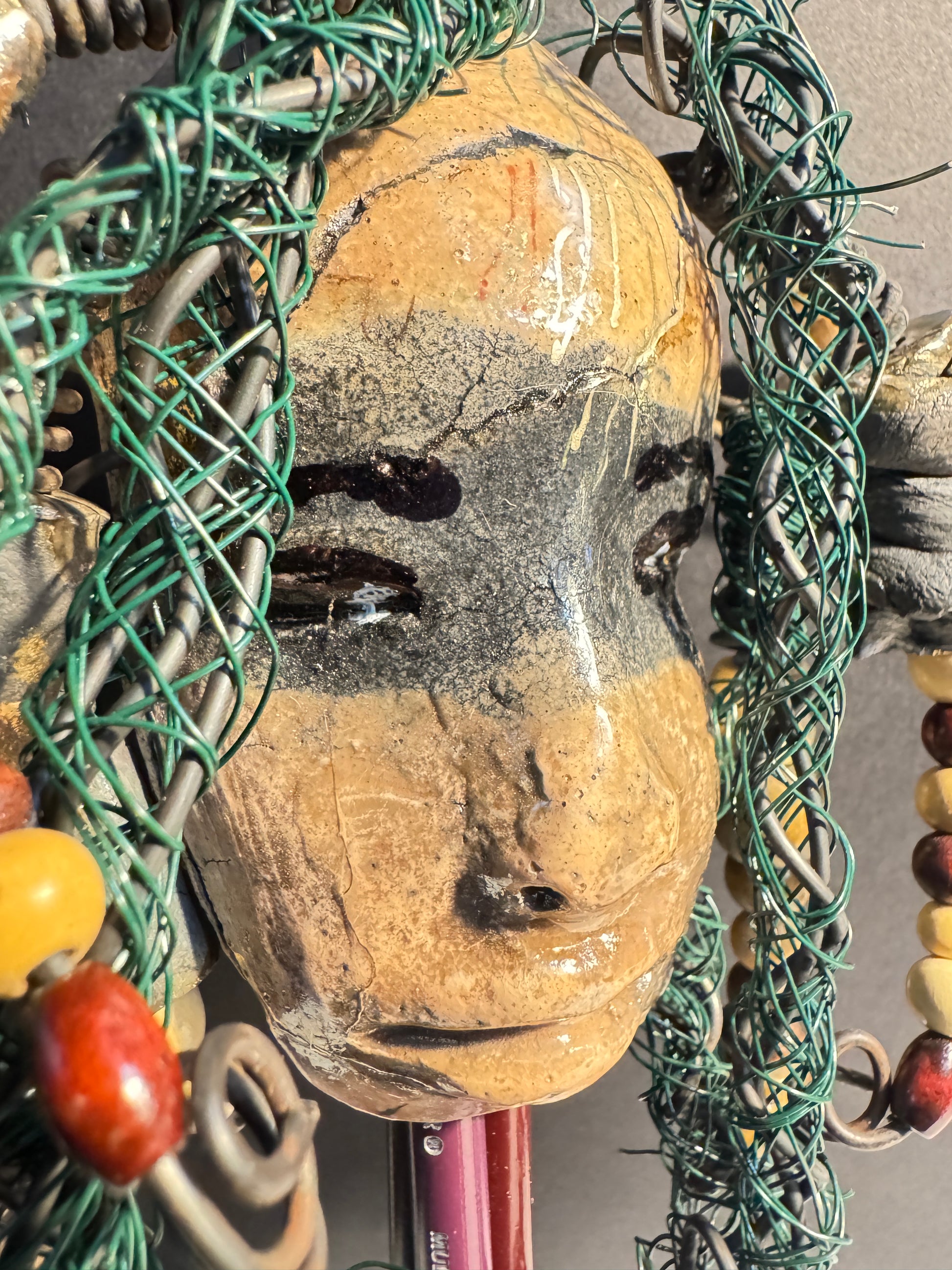 Decorative mixed media raku fired  mask  surrounded with green hair and wooden beads on a gray background
