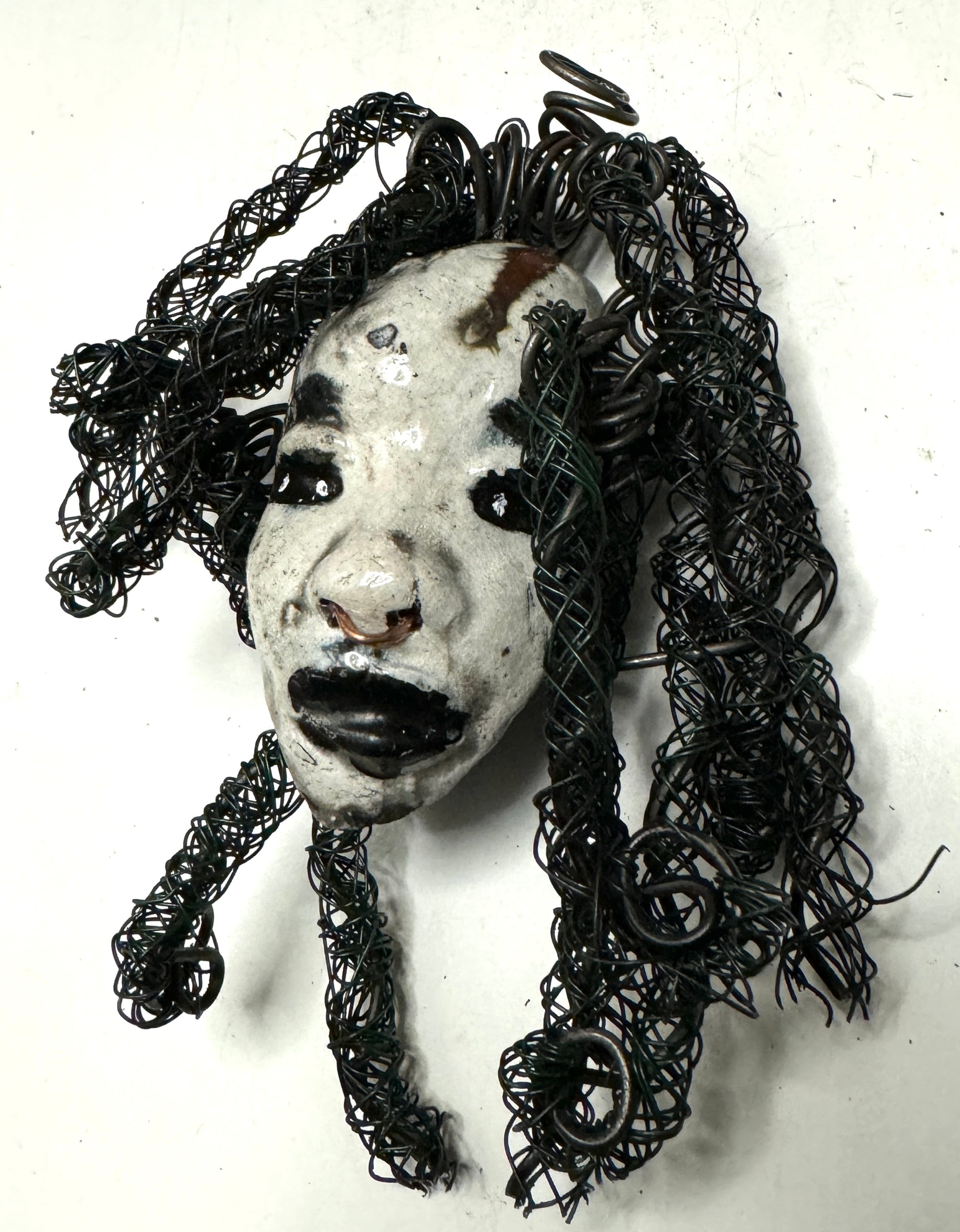 Bongani is a 4x 6” raku-fired mask featuring a pristine off-white color palette. Her intricately detailed hair is composed of nearly 15 feet of 24 gauge wire, delicately adorned. Set in a backdrop of nature, her portrait makes a wonderful addition to any outdoor art collector, or for decorating the home.