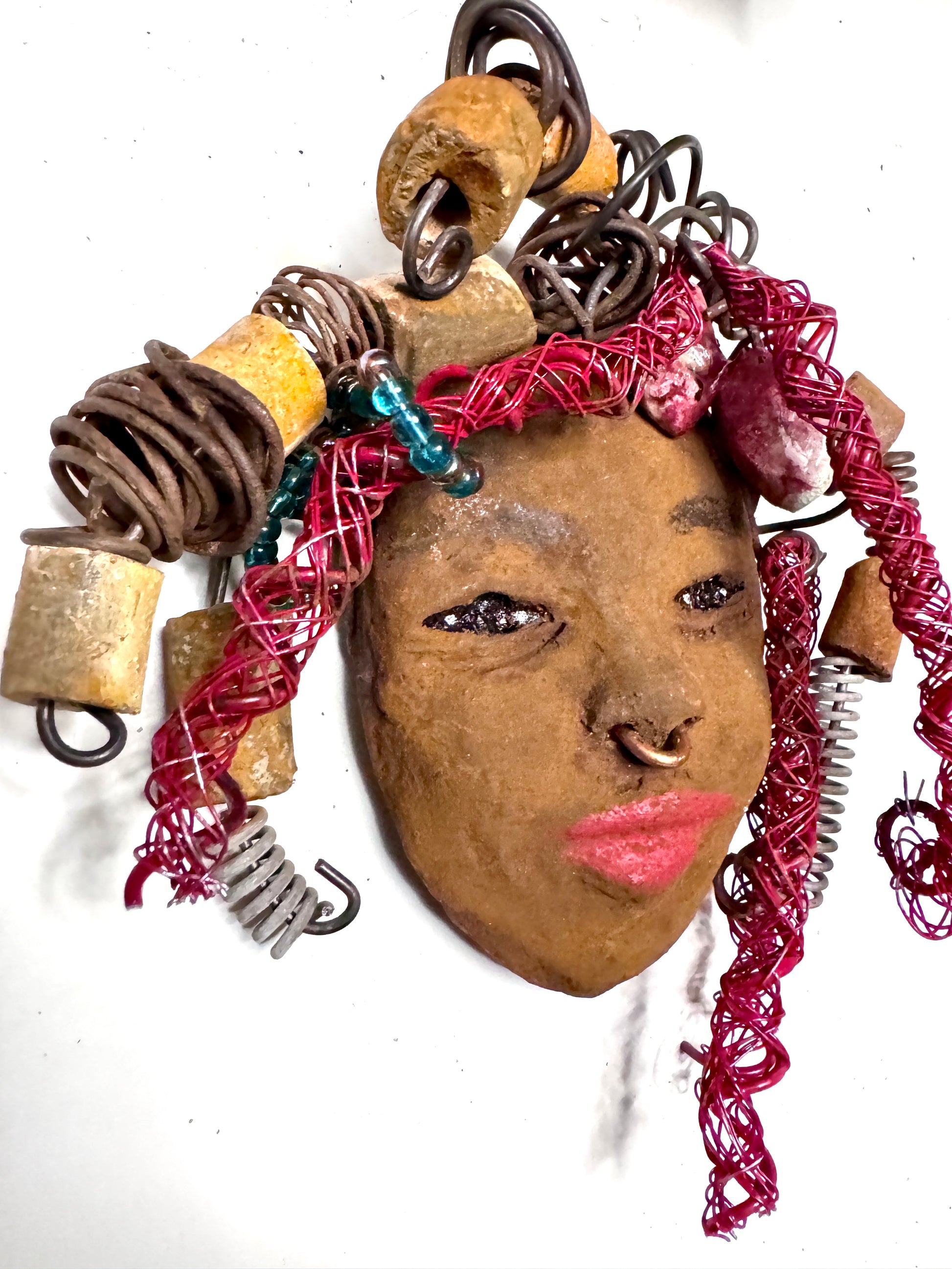 At 5" x 6" in size, Ola makes a stunning addition to walls, trees, and shadow boxes. His signature red braided hair is ornamented with handcrafted Raku beads, while his skin has a warm honey brown hue. Each piece is equipped with over 20 feet of top-notch 16 & 24-gauge wire in the hair. This fashionable sculpture will bring a modern flair to any room - simply place it in a shadow box and enjoy!  