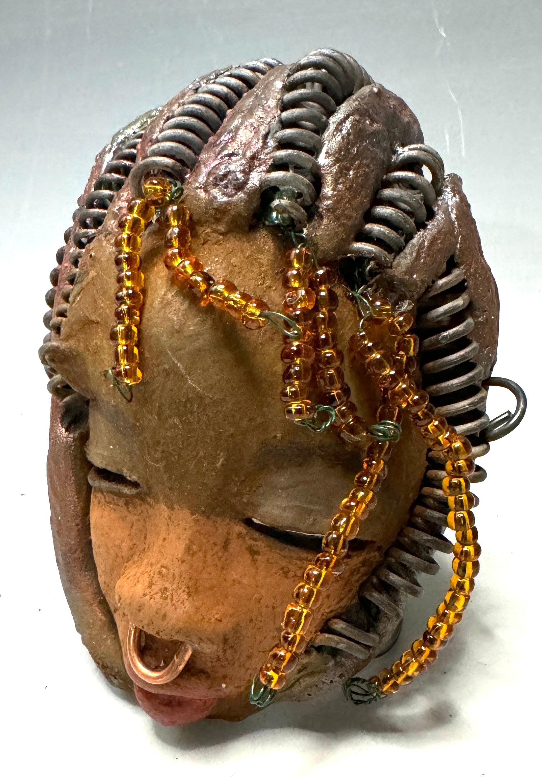 Kenya weighs 5 oz and is 4" by 3" in diameter. Her hair is coppered braided, her complexion is a light gray-blue, and her lips are black. She is a perfect item to start with from the HerDew mask collection. Shadowbox not included.