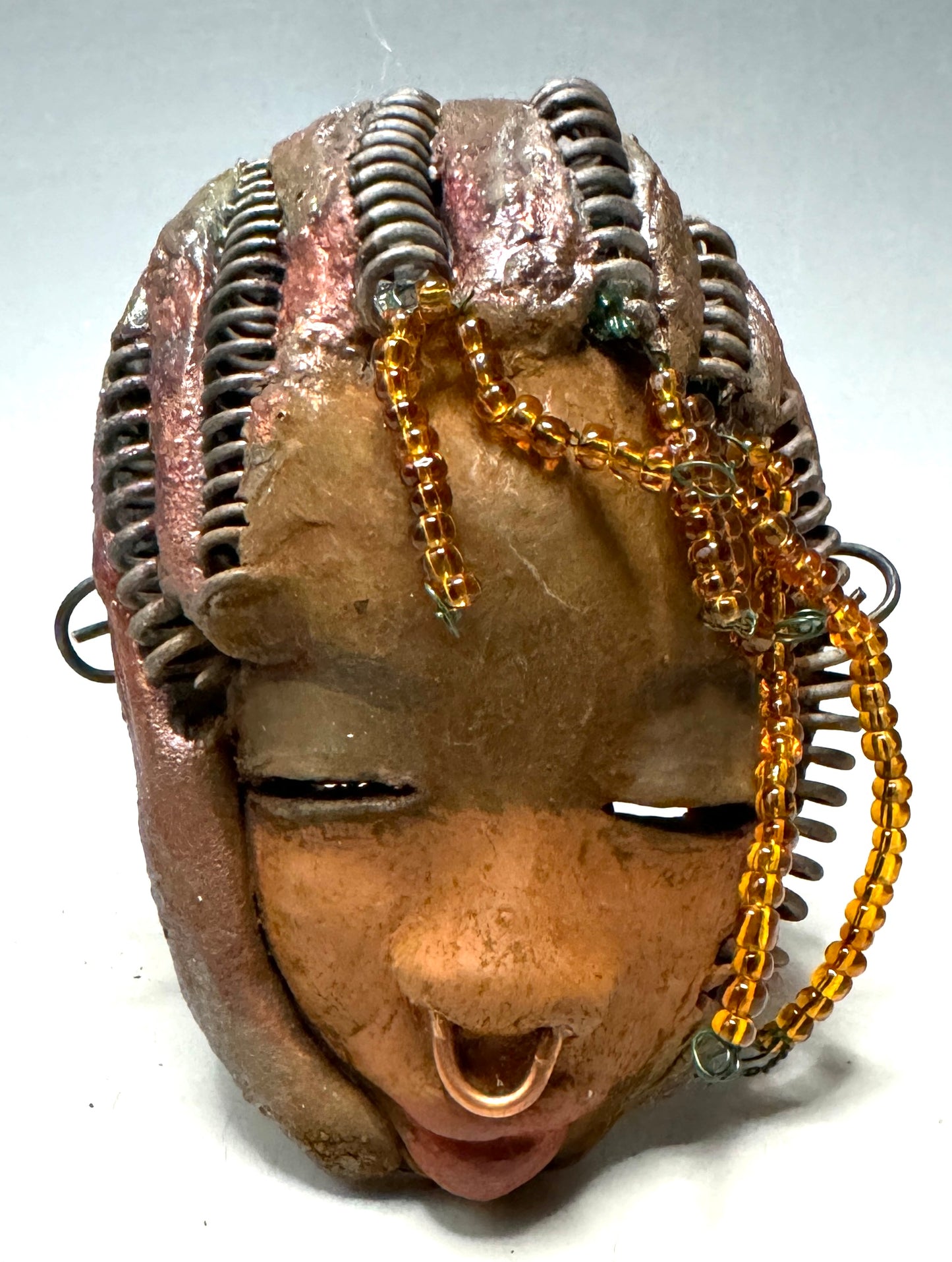 Kenya weighs 5 oz and is 4" by 3" in diameter. Her hair is coppered braided, her complexion is a light gray-blue, and her lips are black. She is a perfect item to start with from the HerDew mask collection. Shadowbox not included.