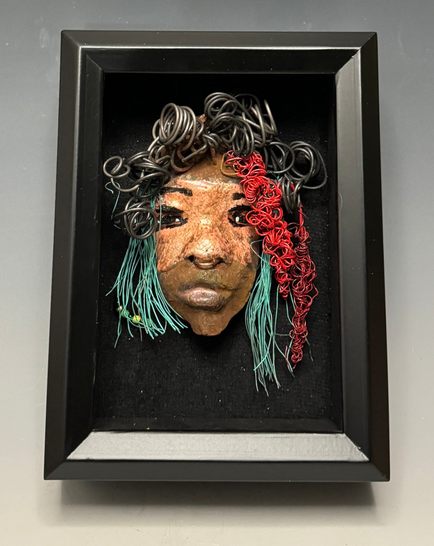 Dakari is an eye-catching two tone tribal raku mask, measuring 4 x 7" and weighing 6 oz. This mask is finished with a stunning blue  and red hair. Dakari also features a copper nose ring. Shadowbox is not included.