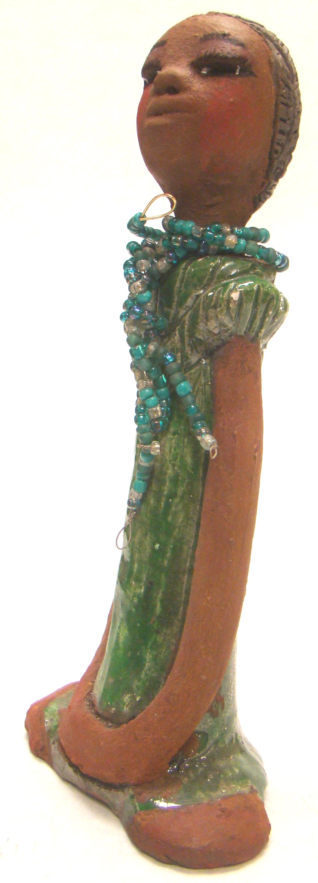      Fatou stands 9" x 4.5" x 2" and weighs 1.03 lbs.     She has a lovely honey brown complexion and long loving arms.     Fatou has an emerald glazed dress with a strand of multicolored beads.     Her hair is raku smokey black and is etched in clay.     Fatou is eye catching and will grace your surroundings.