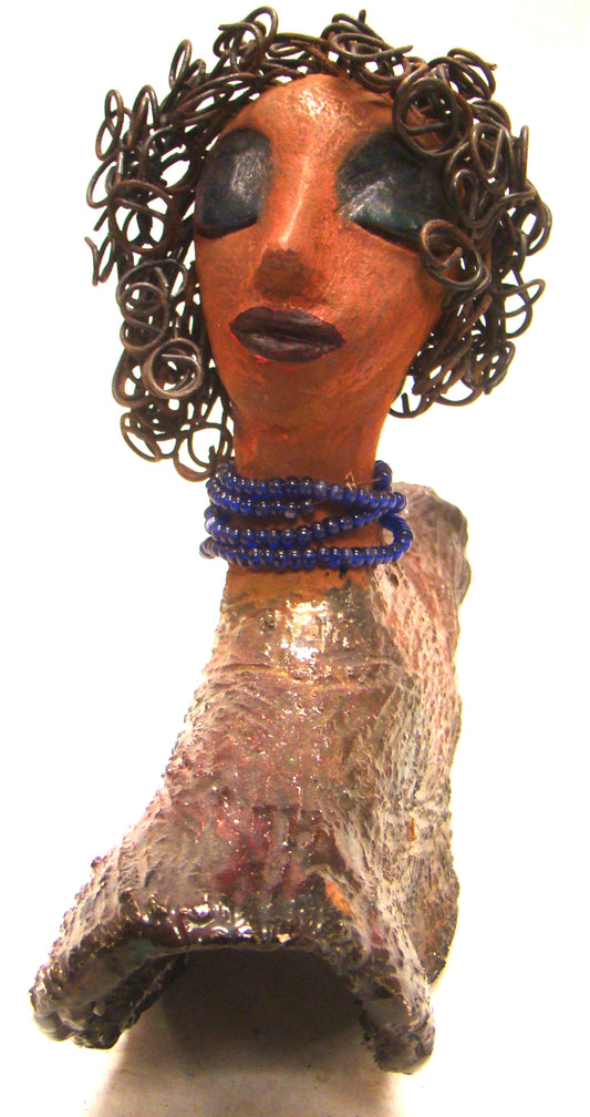 Helen stands 8" x  8" x 3" and weighs 2.06 lbs. She has a lovely honey brown complexion. Helen has a metallic copper glaze on her textured robe. Her blue eye shadow matches the blue strand of beads around her neck. Helen has over 20 feet of curly wire hair. Helen is somewhat angelic! Give Helen a prominent place in your home!