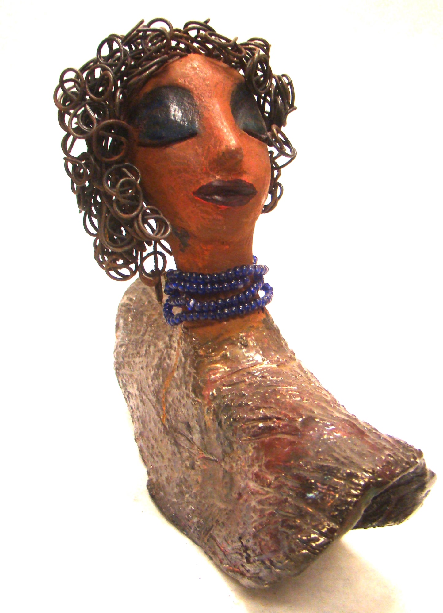 Helen stands 8" x  8" x 3" and weighs 2.06 lbs. She has a lovely honey brown complexion. Helen has a metallic copper glaze on her textured robe. Her blue eye shadow matches the blue strand of beads around her neck. Helen has over 20 feet of curly wire hair. Helen is somewhat angelic! Give Helen a prominent place in your home!