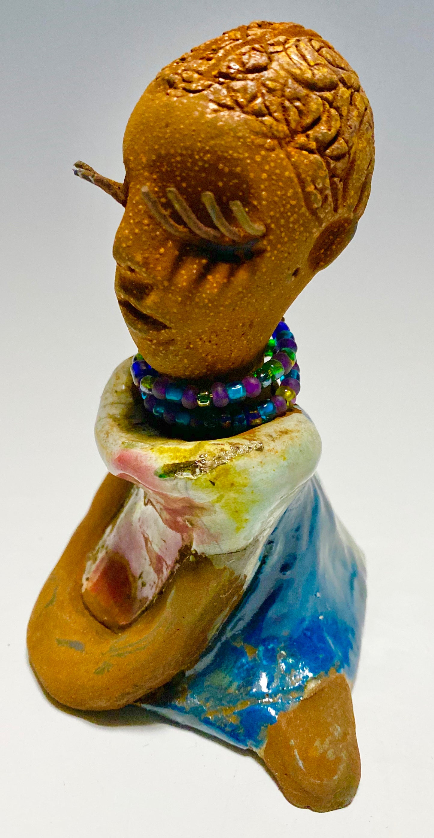 Riley stands 5" x 5”x 3" and weighs  11 ozs.  Riley has a lovely multicolored glossy dress with a matching beaded necklace.  She has long lashes!  Riley appears to sit in a yoga pose. Her long arms rest at her side.