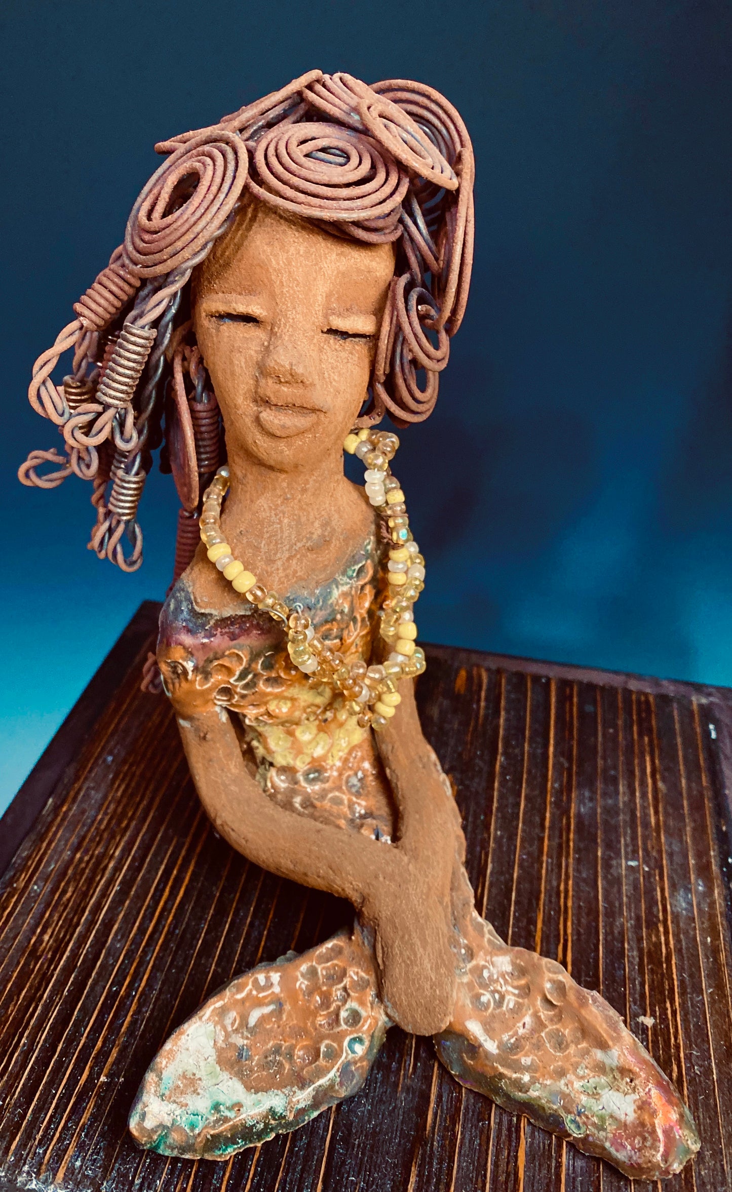 Meet Isabella the Mermaid! Isabella stands 7' x 4" x 6" and weighs 1.08 lbs.. Isabella  has a lovely brown complexion. Her long loving arms are crossed in her lap. Isabella has over 20 feet of  wire hair. It took over two hours to fix her hair! Isabella has a metallic yellow swimsuit with flashes of copper. She wears a yellow beaded necklace. Isabella appears to have something on her mind! Give Isabella a special space in your home!