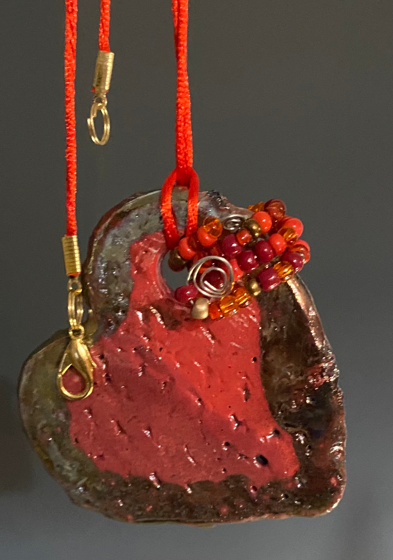 Have A Heart! Each heart pendant is handmade with love! It is 3"x 3" and weighs approx. 3ozs. This pendant has a red violet and gold metallic raku glazes that renders a unique translucent  patina. The heart has a textured pattern . Both sides are  are different and equally beautiful! It holds a spiral of red mini beads on a spiral copper wire. This pendant has a nice 12" red rattail cord!