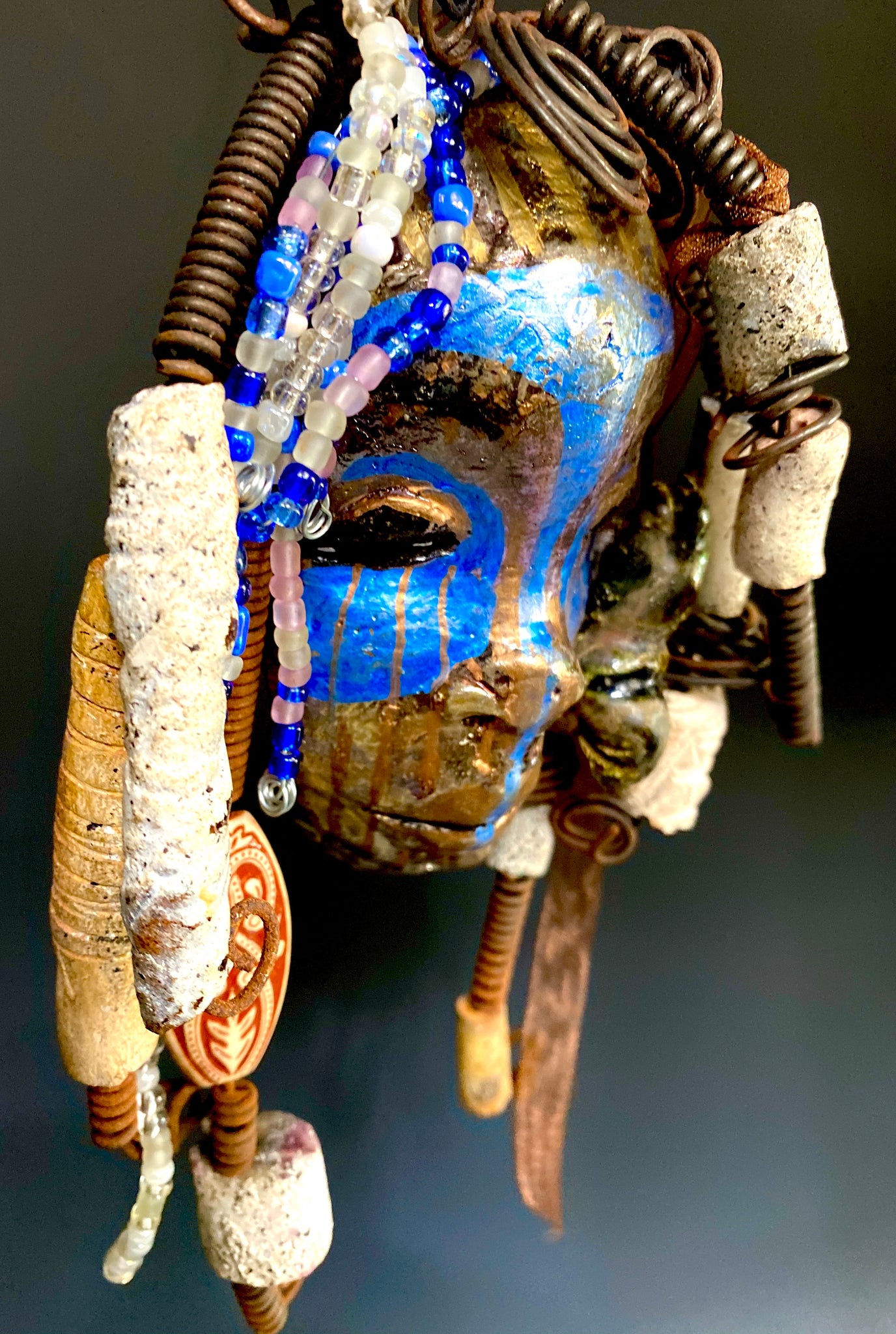 I started making mask soon after seeing authentic African artwork at the Smithsonian Museum of African Art. I was in total awe. I was inspired by my visit there..  Haze has a multi colored blue tone  metallic copper complexion. She is 7" x 5" and weighs 10 ozs. Haze  has  over 50 mini beads and handmade raku beads. Haze has over 4 feet of 16 gauge wire hair.