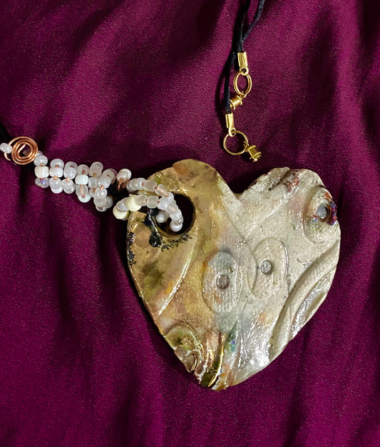 Have A Heart ! Each heart pendant is handmade with love! It is 3"x 3" and weighs approx. 3ozs. This pendant has a toasty white copper metallic raku glazes that renders a unique translucent  patina. The heart has a textured pattern . Both sides are  are different and equally beautiful! It holds a spiral of white  mini beads on a spiral copper wire. This pendant has a nice 12"  black rattail cord!