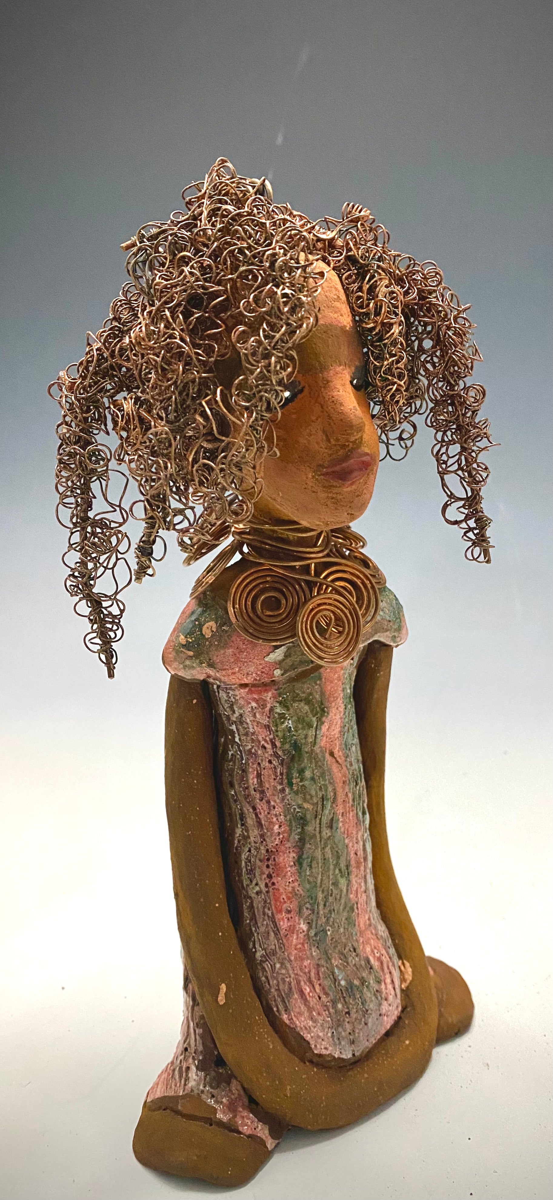 " I am really pleased with Jada's copper coiled necklace and her new wire hair. It complements her well!" Jada stands 9" x 4.5" x 2.5" and weighs 1 lb. She has a lovely two tone honey brown complexion. Jada's dress is a metallic glaze with copper red stripes. She has her long loving arms resting at her side. Find a place in your space for Jada!