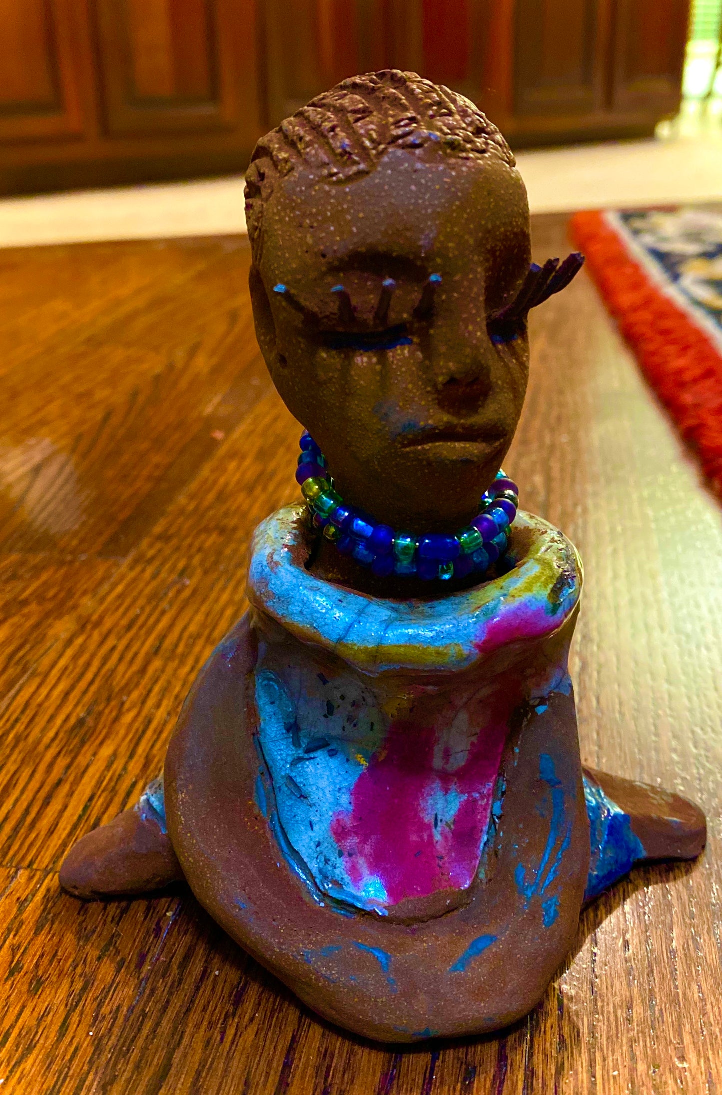 Riley stands 5" x 5”x 3" and weighs  11 ozs.  Riley has a lovely multicolored glossy dress with a matching beaded necklace.  She has long lashes!  Riley appears to sit in a yoga pose. Her long arms rest at her side.