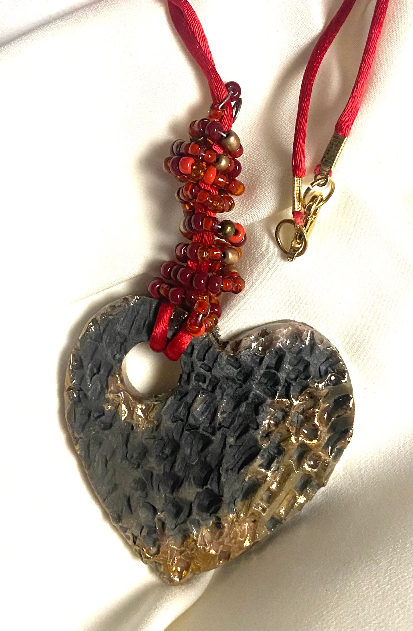 Have A Heart ! Each heart pendant is handmade with love! It is 3"x 3" and weighs approx. 3ozs. This pendant has a copper gold metallic raku glazes that renders a unique translucent  patina. The heart has a textured pattern . It holds a spiral of red mini beads on a spiral copper wire. This pendant has a nice 12" red suede cord!