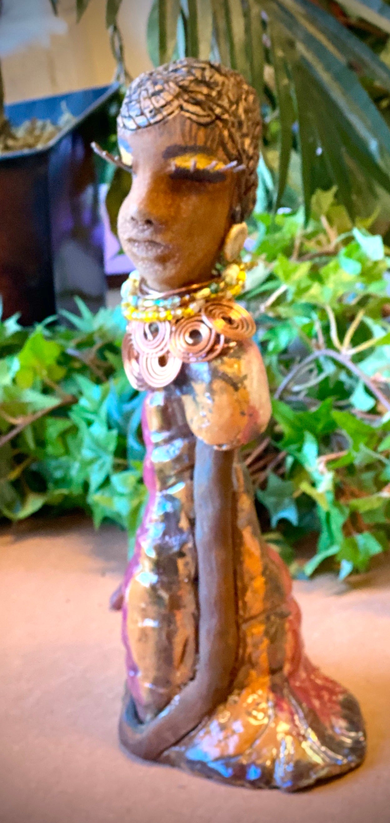 Keeba  long loving arms rest beside her multicolored metallic dress. She wears a spiral copper necklace. Keeba  is a sophisticated lady that will grace your home.