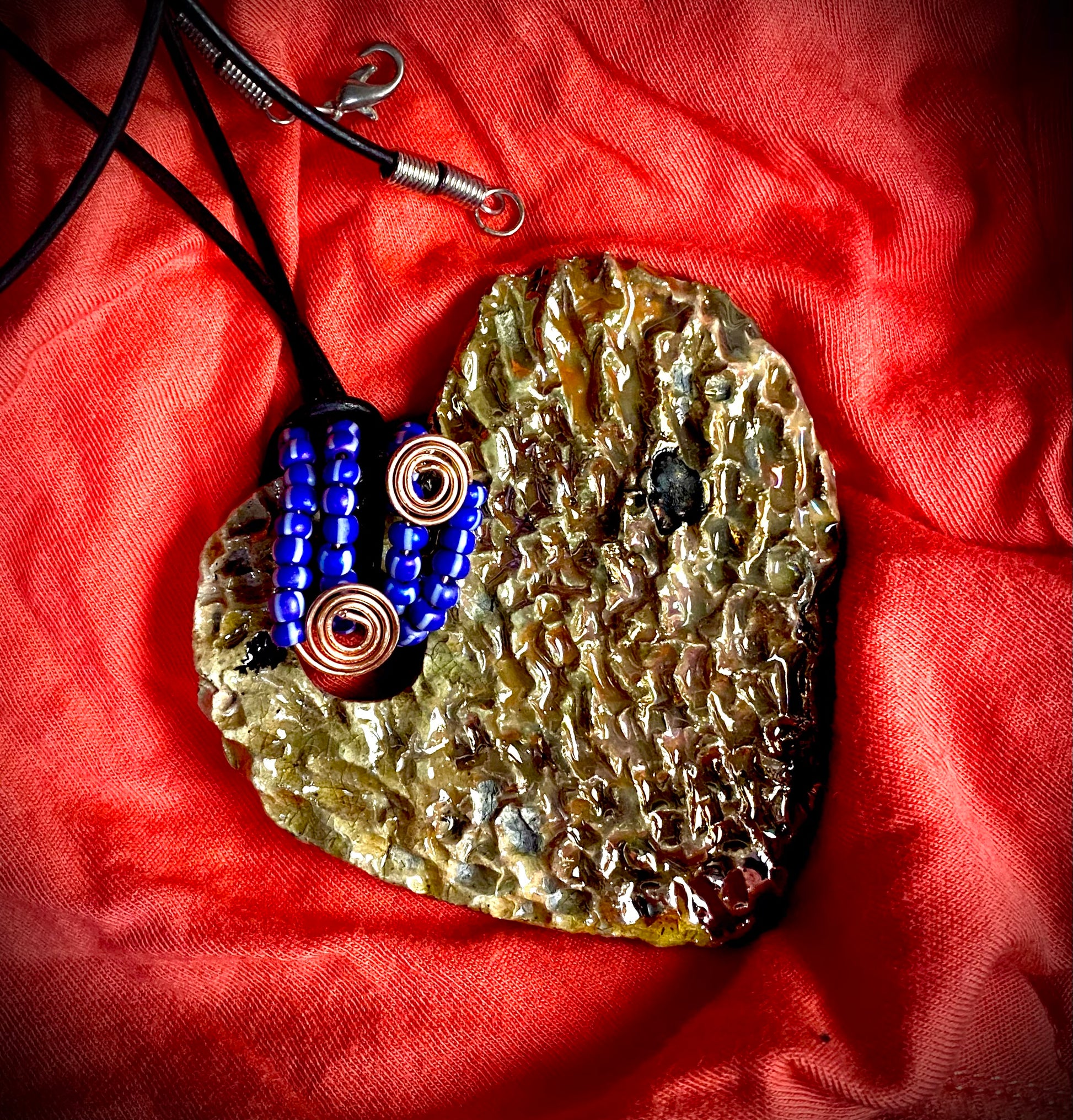 Have A Heart ! Each heart pendant is handmade with love! It is 3"x 3" and weighs approx. 3ozs. This pendant has a golden white metallic raku glazes that renders a unique translucent  patina. The heart  has a high textured  surface. It holds a spiral of blue mini beads on a spiral copper wire. This pendant has a nice 12" black suede cord!