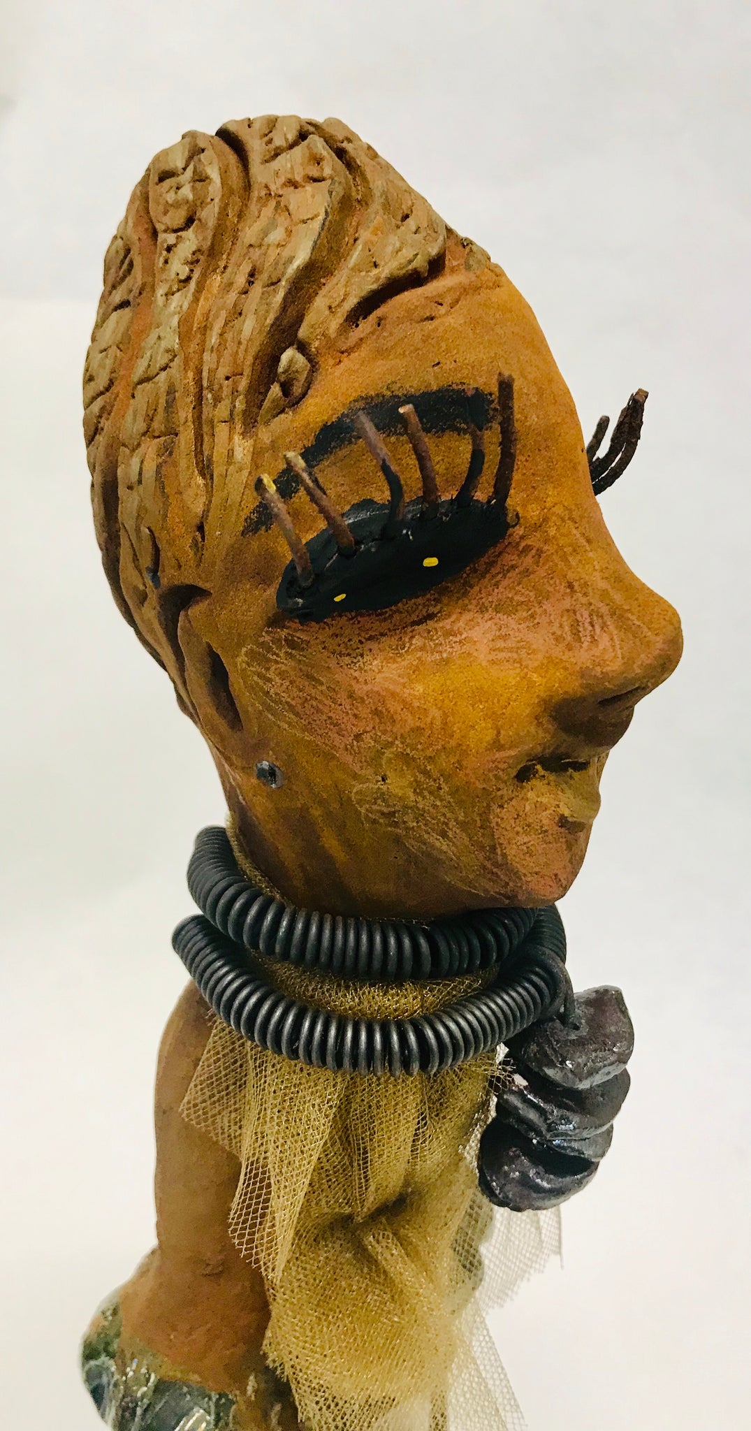Trinity stands 14" x 4" x 4" and weighs 2.7 lbs. She has a lovely honey brown complexion with  reddish brown lips. She has a braided hairstyle.  Trinity has a colorful metallic green antique copper glazed dress. She wears a spiral wire necklaces with raku beads underneath an antique gold tulle.. With long lashes and eyes wide opened, Trinity has hopes of finding a new home.  