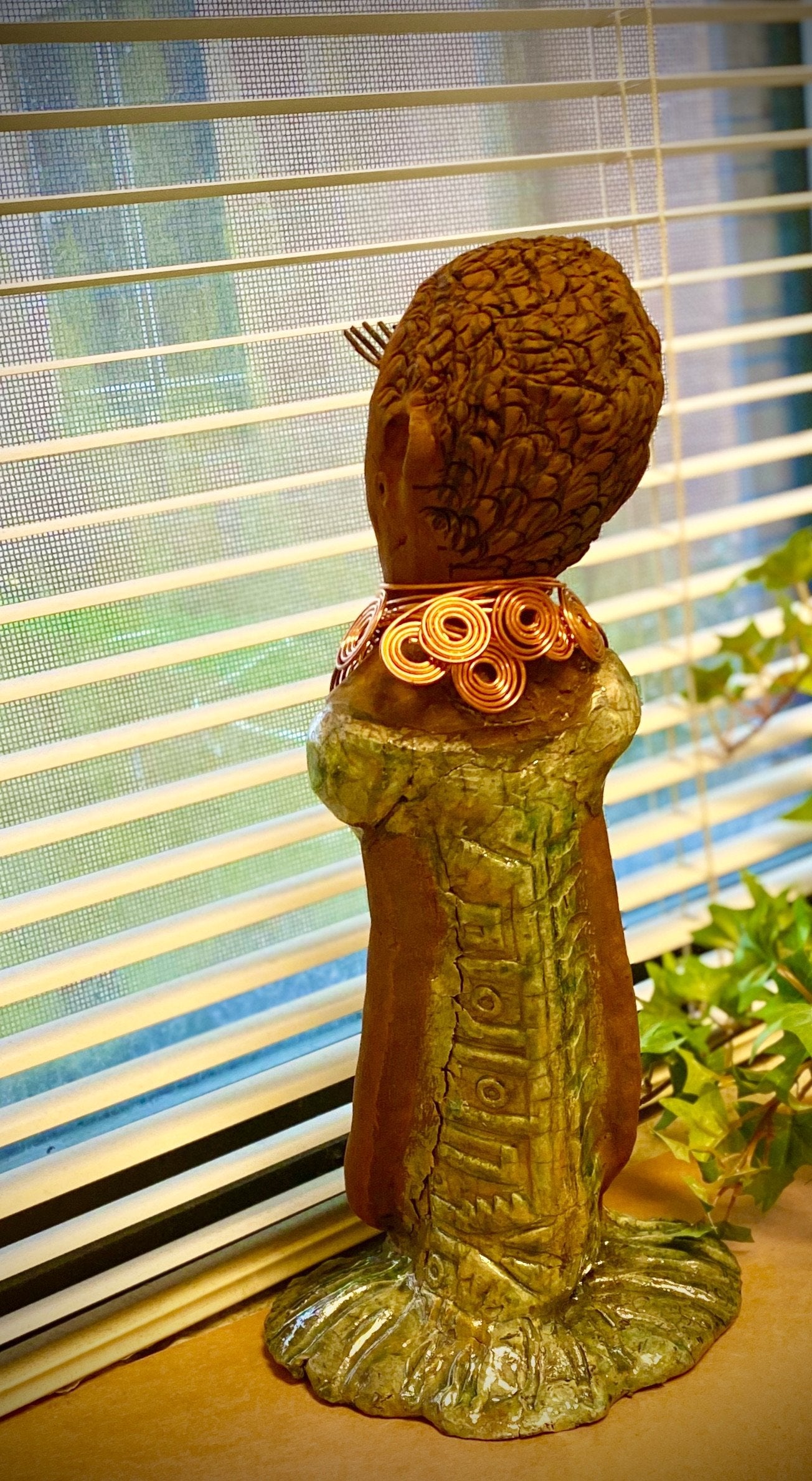 Gabrielle  stands 14" x 6" x 5.5" and weighs 2.15 lbs. She has a lovely honey brown complexion with green eye shadow. Her hairstyle is etched in clay with tribal markings.  Gabrielle  long loving arms rest beside her alligator green dress. She wears a spiral copper necklace. Gabrielle  is a sophisticated lady that will grace your home.