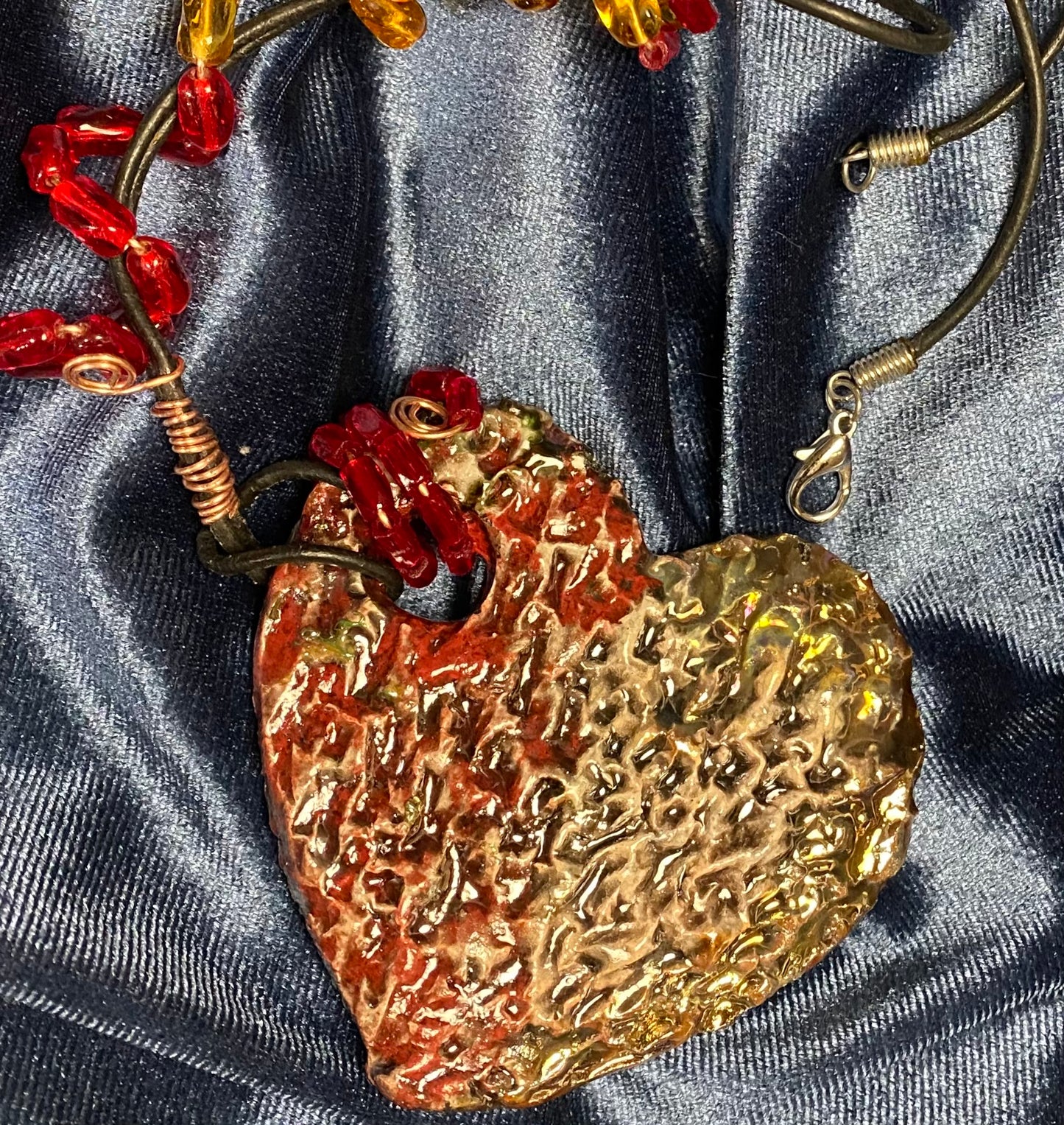 Have A Heart ! Each heart pendant is handmade with love! It is 3"x 3" and weighs approx. 3ozs. This pendant has a red and gold metallic raku glazes that renders a unique translucent  patina. The heart has a textured pattern . It holds a spiral of amber and red mini beads on a spiral copper wire. This pendant has a nice 12" black suede cord!