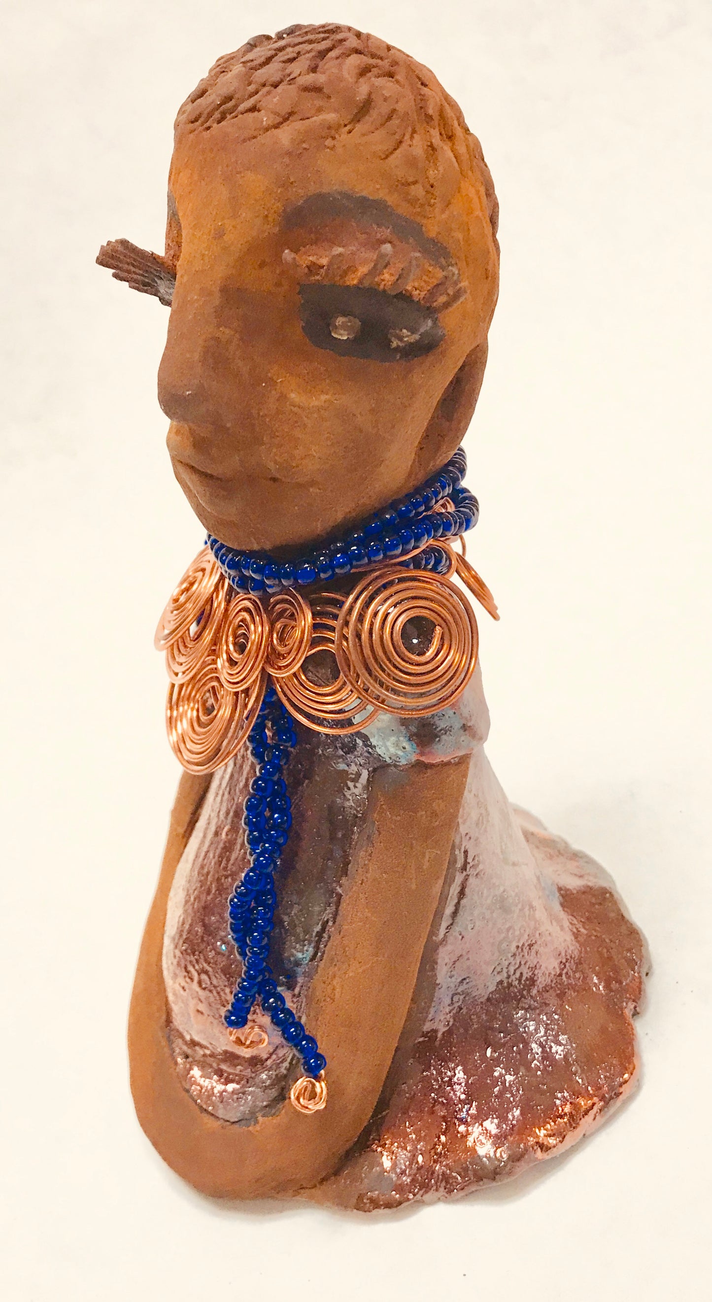 Tattayana stands 8" x 4.5" x 5" and weighs 1.02  lbs. She has a lovely honey brown complexion with reddish brTattayanaown lips. She has a short braided hairstyle.  Tattayana has a colorful metallic antique copper glazed dress. She wears spiral copper wire necklaces on top of an aqua blue beaded collar.  Tattayana has her long loving arms rest at her side. With eyes wide opened,Tattayana  has hopes of finding a new home.