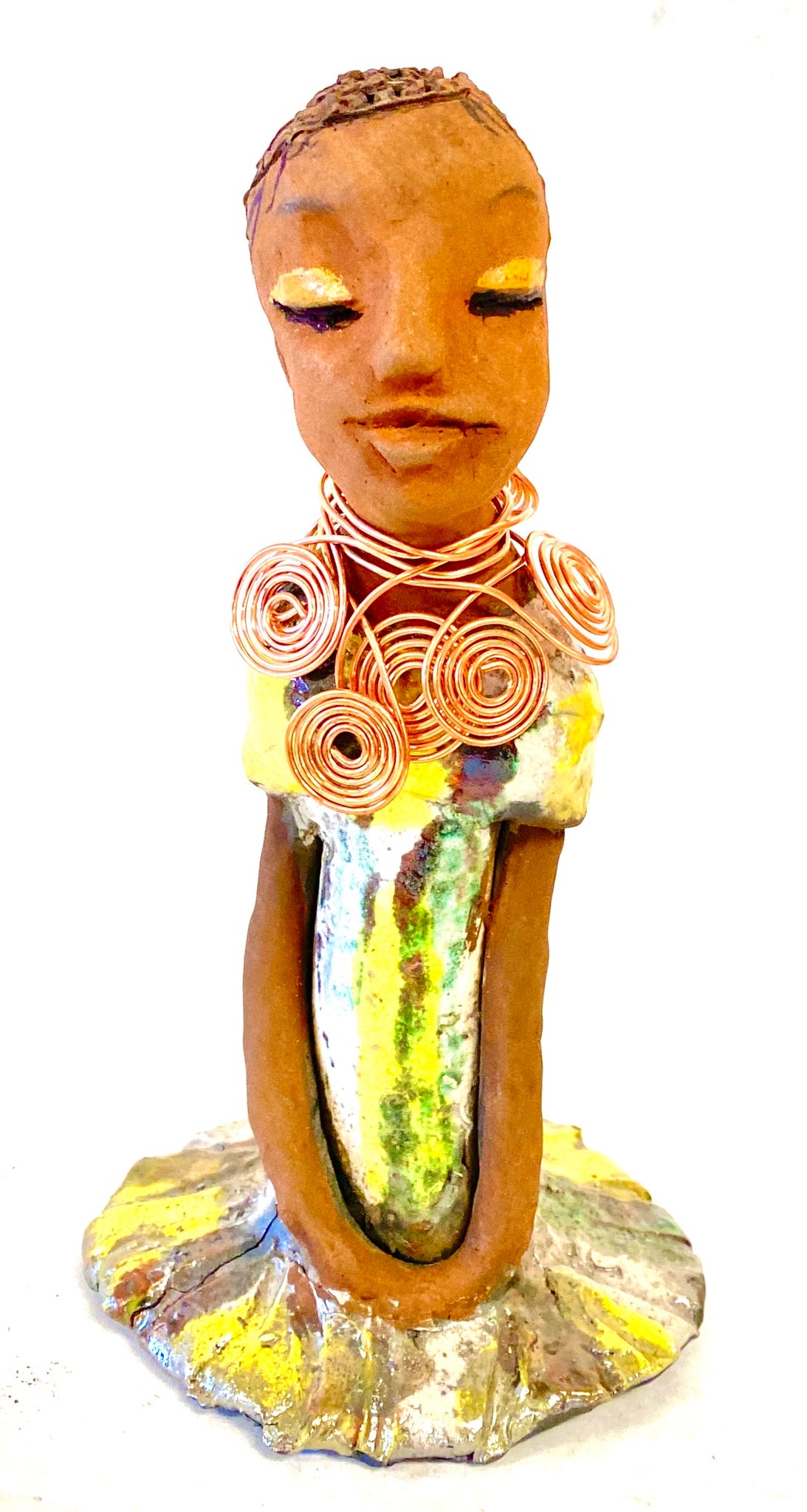 Meet Trisha! Trisha stands 9.5" x 5”x 5" and weighs  1.3 lbs.  Trisha has a lovely glossy yellow  green dress with a copper spiral necklace.   Her hair is etched in clay. Her long arms rest at her side. Trisha is at a special low price. This makes her an excellent starter piece from the Herdew Collection!