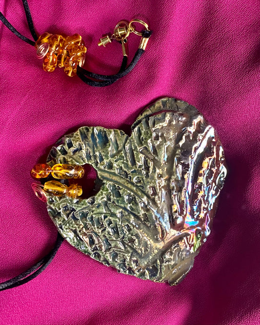 Have A Heart ! Each heart pendant is handmade with love! It is 3"x 3" and weighs approx. 3ozs. This pendant has an alligator green and gold metallic raku glazes that renders a unique translucent  patina. The heart  has a textured  pattern. It holds a spiral of amber mini beads on a spiral copper wire. This pendant has a nice 12" black suede cord!