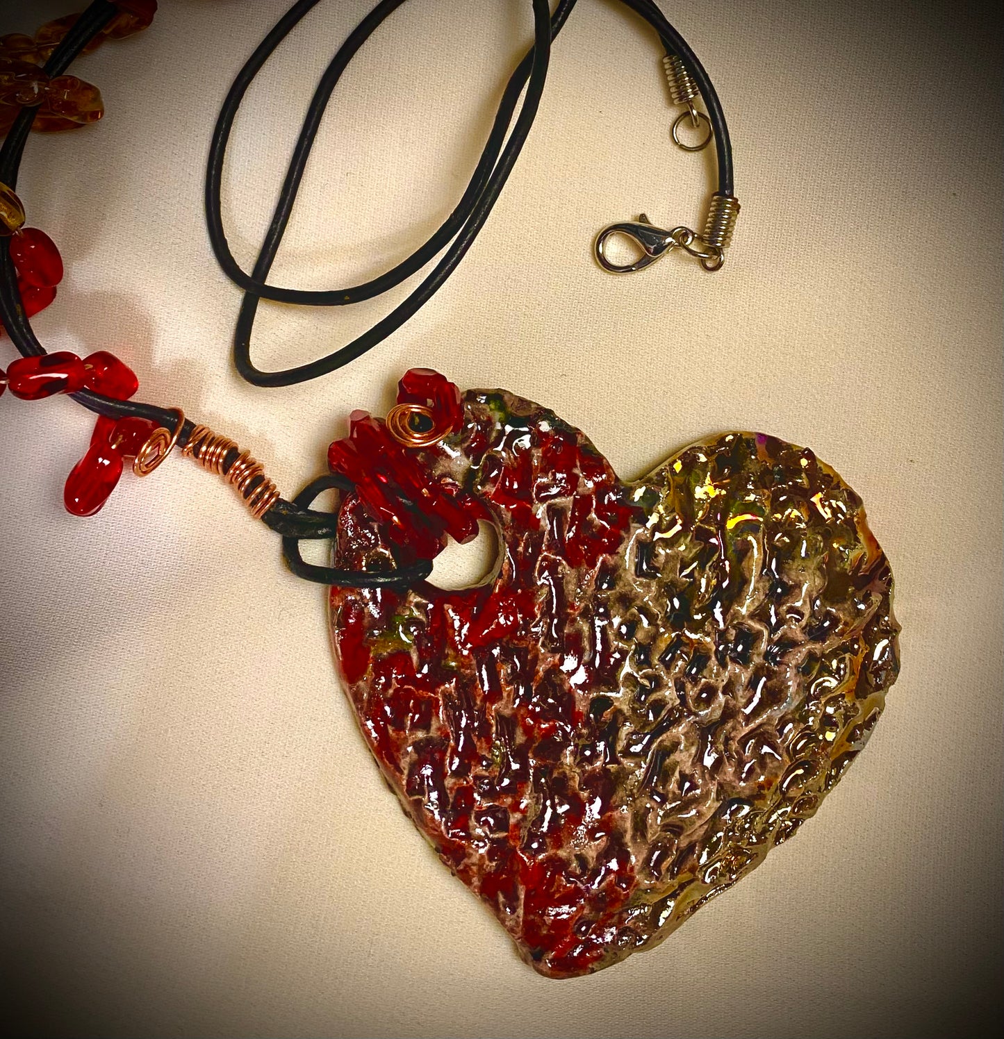 Have A Heart ! Each heart pendant is handmade with love! It is 3"x 3" and weighs approx. 3ozs. This pendant has a red and gold metallic raku glazes that renders a unique translucent  patina. The heart has a textured pattern . It holds a spiral of amber and red mini beads on a spiral copper wire. This pendant has a nice 12" black suede cord!