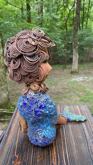 Meet Shelia E.! She is such a Lady I mean Mermaid!    Shelia stands 12" x 10" x 4" and weighs 3.13 lbs. Shelia has a two tone honey brown complexion. She has over 15 feet of spiral wire hair which took over two hours to style. Shelia wears a textured sky blue swimsuit Her layered spiral copper necklace hangs above her long loving arm. Shelia is such a ladylike Mermaid. She sits tall and proud. Compare her to Harmony the mermaid. Give Shelia or Harmony a special place to sit in your home!