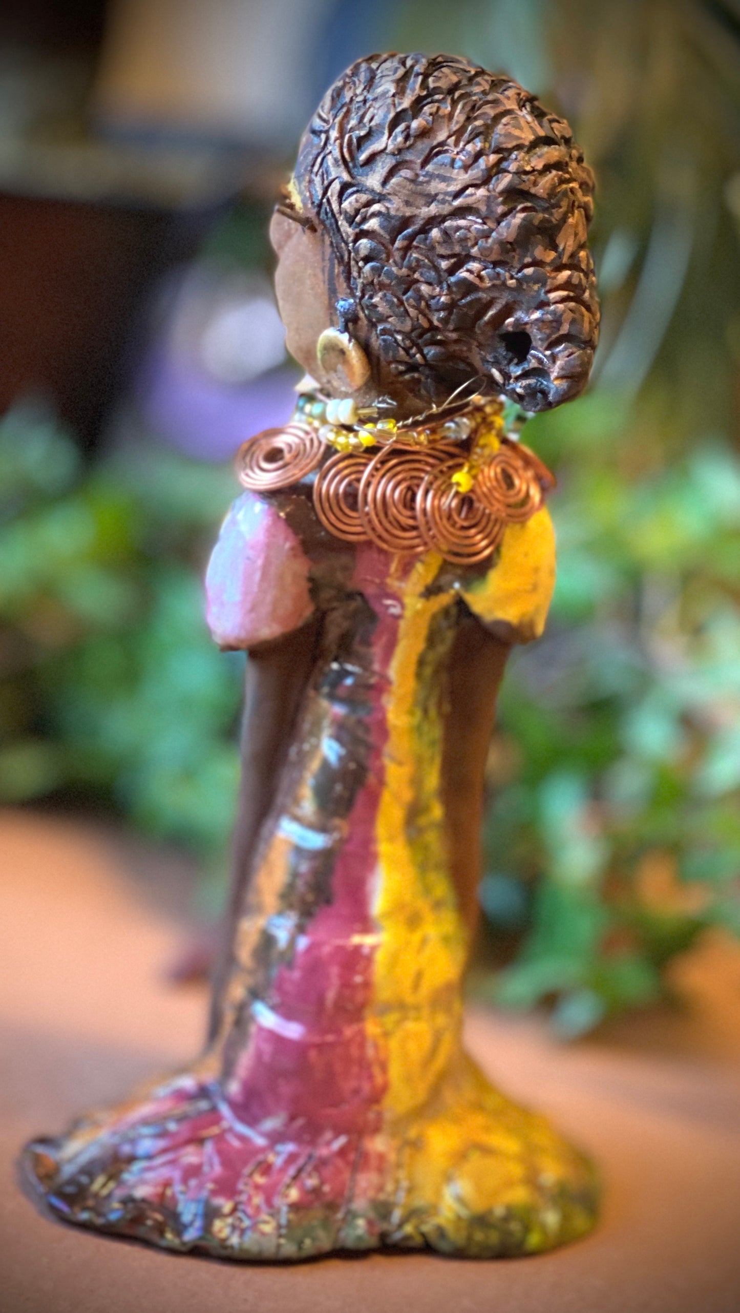 Keeba  long loving arms rest beside her multicolored metallic dress. She wears a spiral copper necklace. Keeba  is a sophisticated lady that will grace your home.