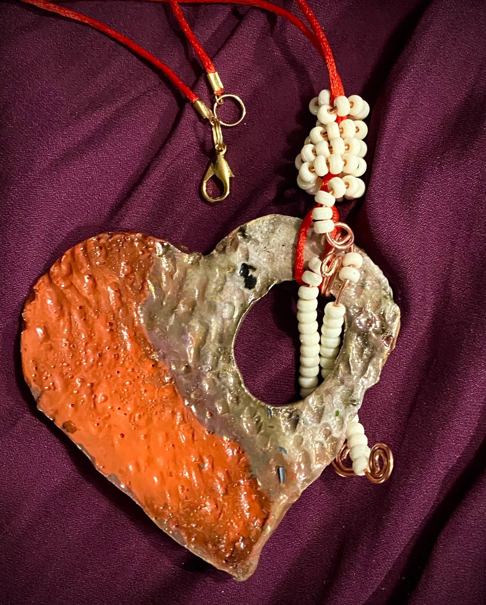 Have A Heart! Each heart pendant is handmade with love! It is 3"x 3"and weighs approx. 3ozs. This pendant has a red,orange, white and copper metallic raku glazes that renders a unique translucent  patina. The heart has a textured pattern . Both sides are  are different and equally beautiful! There is a spiral white mini beads on copper in the center. This pendant has a nice 12" red adjustable rattail cord!