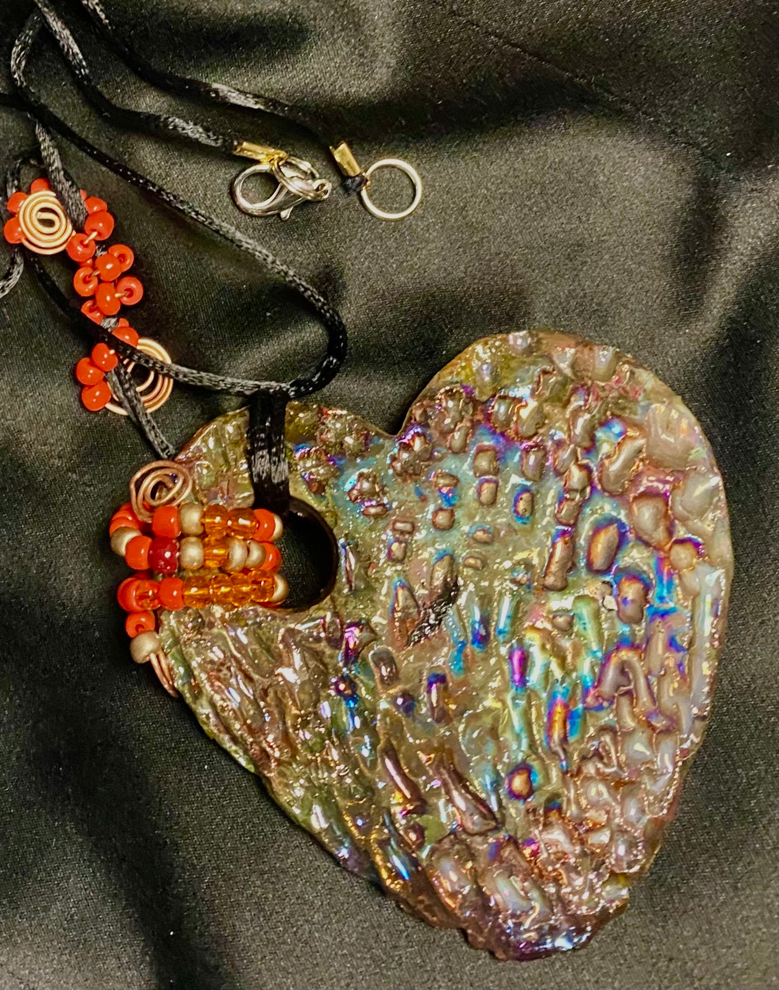  Have A Heart ! Each heart pendant is handmade with love! It is 3"x 3" and weighs approx. 3ozs. This pendant has a copper gold metallic raku glazes that renders a unique translucent  patina. The heart has a textured pattern . It holds a spiral of amber and red mini beads on a spiral copper wire. This pendant has a nice 12" black suede cord!
