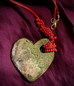  Have A Heart ! Each heart pendant is handmade with love! It is 3"x 3" and weighs approx. 3ozs. This pendant has a toasty copper metallic raku glazes that renders a unique translucent  patina. The heart has a textured pattern . Both sides are  are different and equally beautiful! It holds a spiral of red violet mini beads on a spiral copper wire. This pendant has a nice 12" red suede cord!