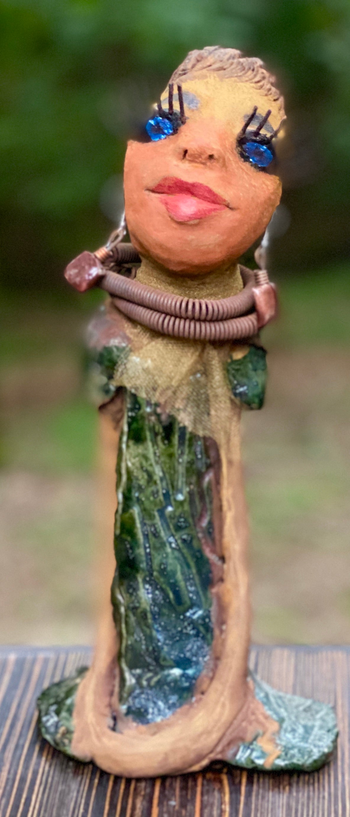 Meet Catera! Catera stands 10" x 4" x 4" and weighs 2.7 lbs. She has a lovely honey brown complexion with  reddish brown lips. She has a braided hairstyle.  Catera has a colorful metallic green antique copper glazed dress. She wears a yellow bead necklace with raku beads. Her long loving arms are resting at her side. With long lashes and eyes wide opened, Catera has hopes of finding a new home.  