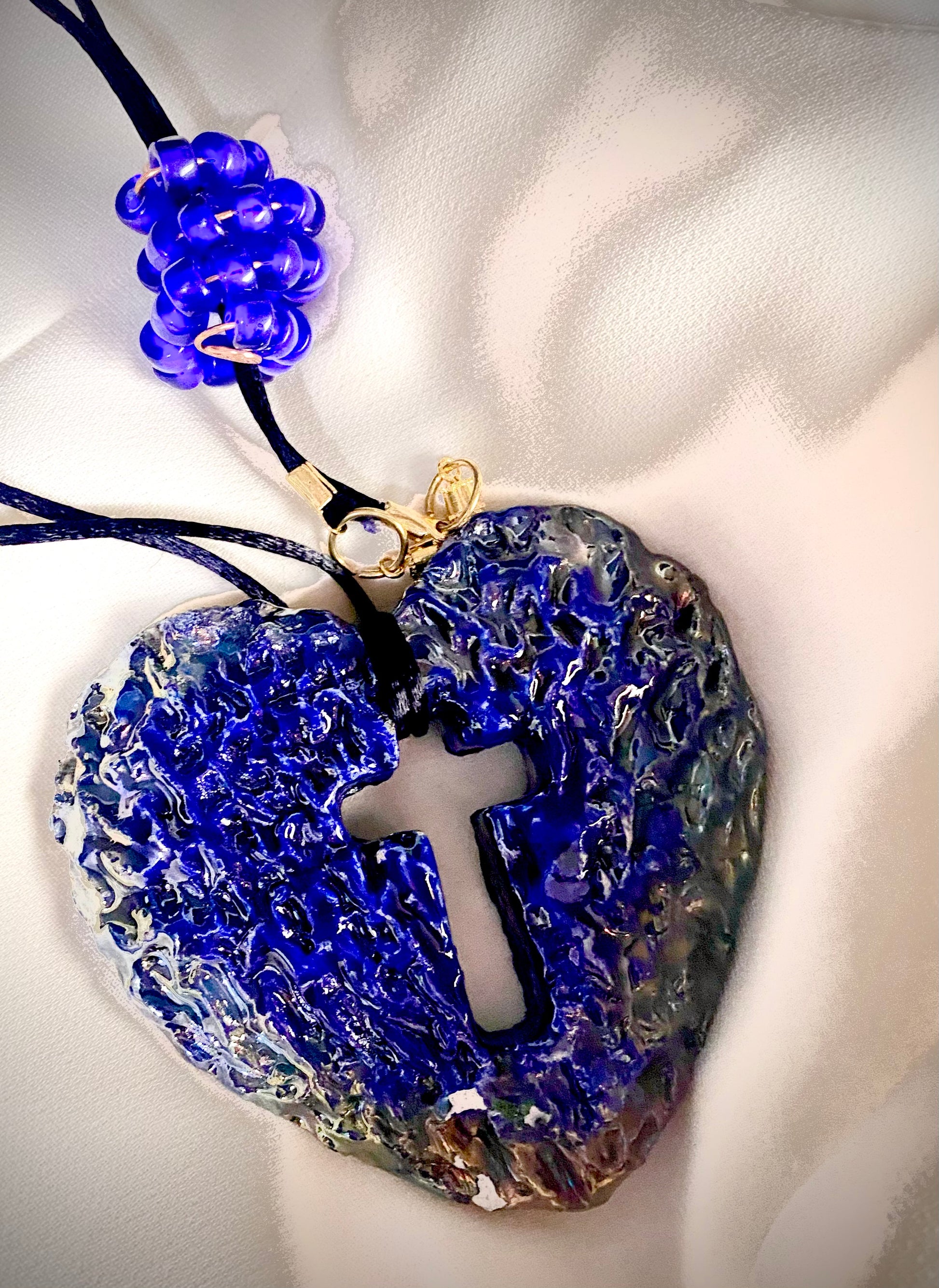  Have A Heart ! Each heart pendant is handmade with love! It is 3"x 3" and weighs approx. 3ozs. This pendant has a royal blue and gold metallic raku glazes that renders a unique translucent  patina. The heart has a cut out cross in the center with a textured  pattern. It holds a spiral of royal blue mini beads on a spiral copper wire. This pendant has a nice 12" black suede cord!