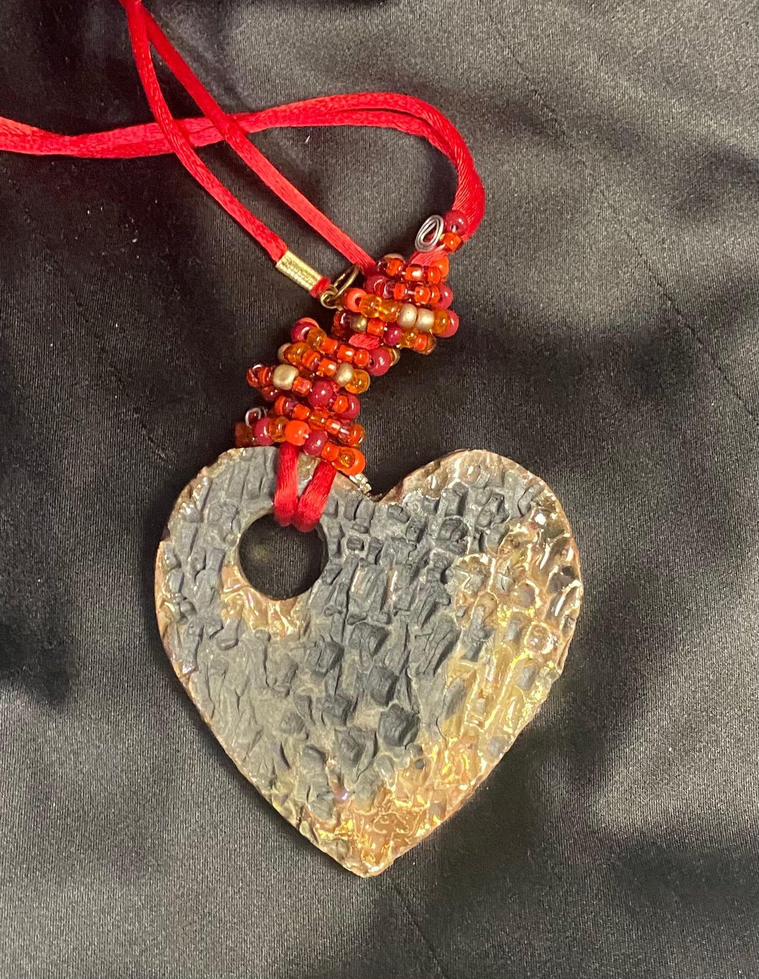 Have A Heart ! Each heart pendant is handmade with love! It is 3"x 3" and weighs approx. 3ozs. This pendant has a copper gold metallic raku glazes that renders a unique translucent  patina. The heart has a textured pattern . It holds a spiral of red mini beads on a spiral copper wire. This pendant has a nice 12" red suede cord!