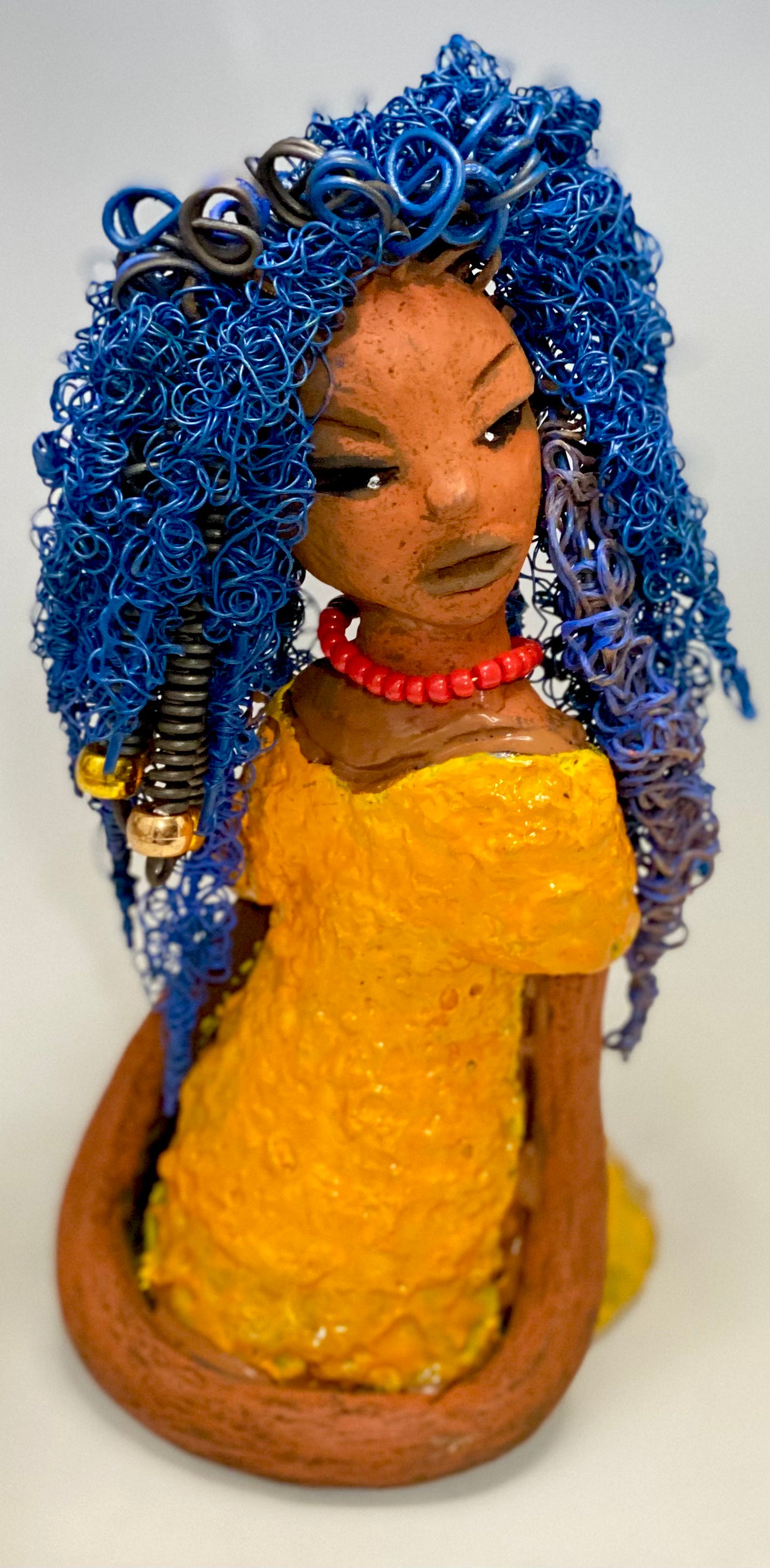 Makeba stands 8" x 5" x 5" and weighs 1.4 lbs. She has a lovely honey brown complexion with cocoa red lips. She has long twisted  blue wire locs hairstyle waist down!  Makeba has a sunset yellow red glazed dress. She has over 75 feet of 16 and 24 gauge blue wire for hair. It took over 5 hours just to do her hair! With  eyes wide opened and a subdue look, Makeba has hope of finding a new home.