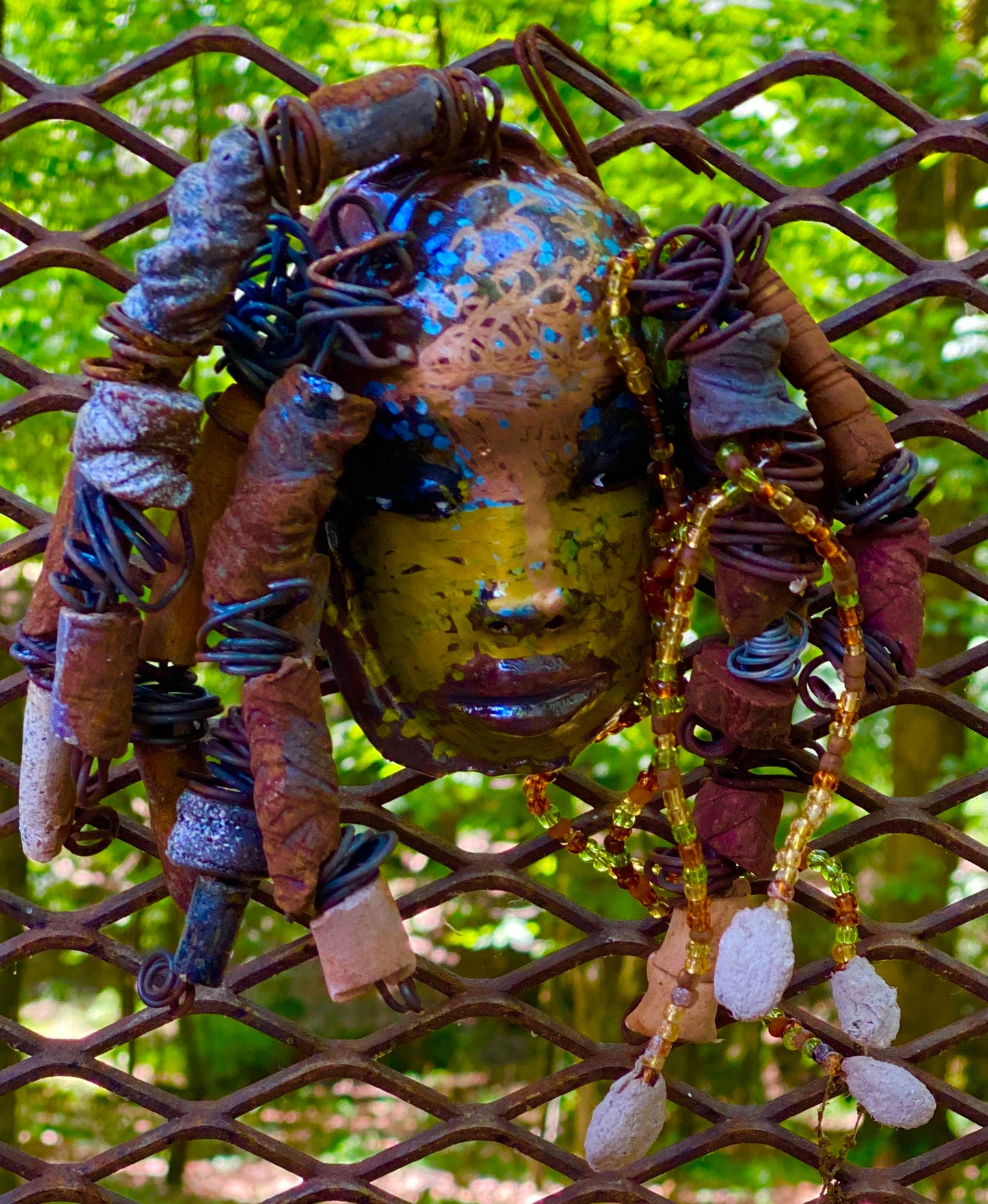 I started making mask soon after seeing authentic African artwork at the Smithsonian Museum of African Art. I was in total awe. Marali means she who listen  was inspired by my visit there.  Marali has a two tone  metallic blue copper gold complexion. She is 7" x 5" and weighs 14 ozs. Marali has  over 20 handmade raku fired beads. She has over 50 mini amber bead twisted as hair. Marali has over 6 feet of  copper coiled 16 gauge wire hair.