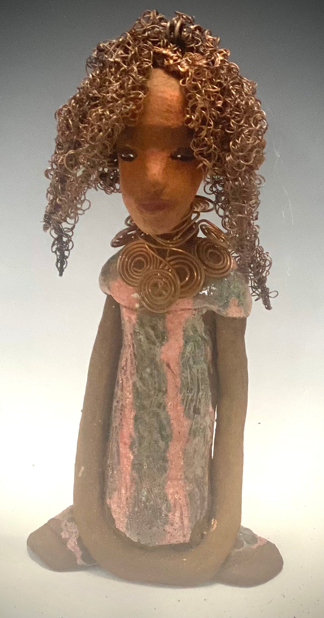 " I am really pleased with Jada's copper coiled necklace and her new wire hair. It complements her well!" Jada stands 9" x 4.5" x 2.5" and weighs 1 lb. She has a lovely two tone honey brown complexion. Jada's dress is a metallic glaze with copper red stripes. She has her long loving arms resting at her side. Find a place in your space for Jada!