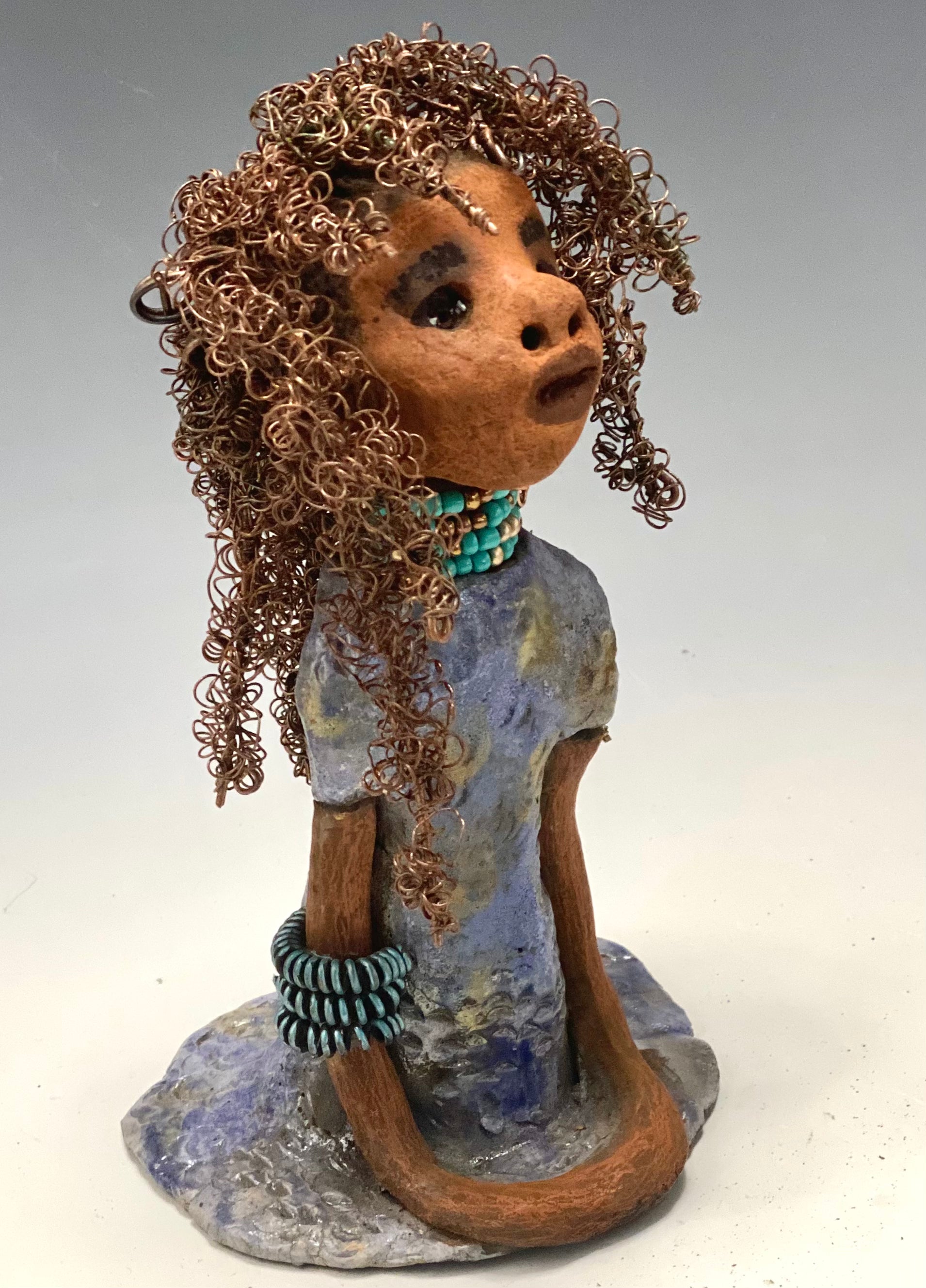 Meet Janae'! She has grown a head full of Hair! Janae' stands 8" x 5" x 4" and weighs 1.03 lbs. She has a lovely honey brown complexion with lovely reddish brown lips. Janae' wears a clay braided hairstyle. Janae' has a colorful metallic blue and gold glazed dress. She wears a blue and antique copper  beaded necklace. With eyes wide opened, Janae' has hopes of finding a new home.  