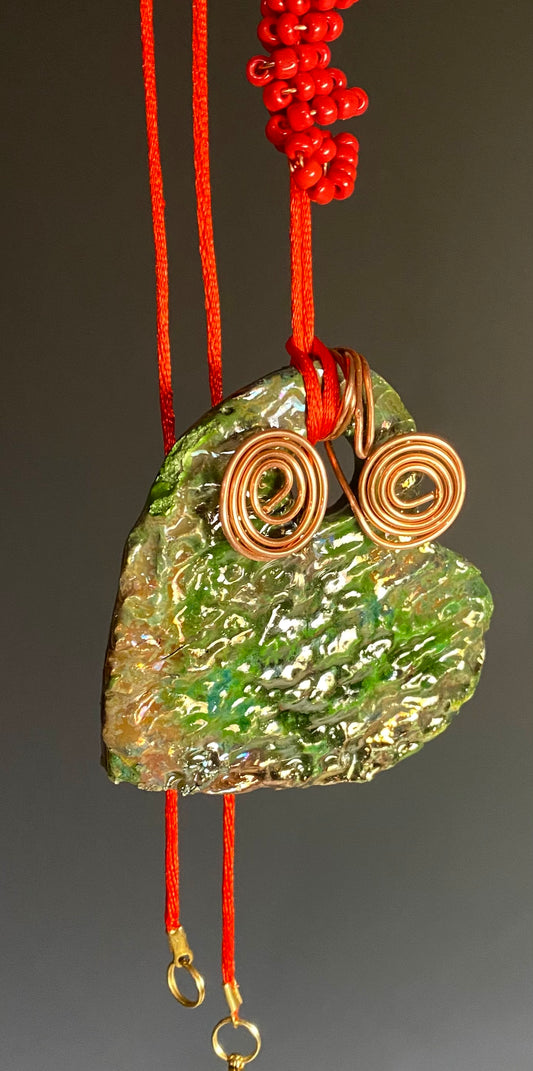 Have A Heart! Each heart pendant is handmade with love! It is 3"x 3"and weighs approx. 3ozs. This pendant has a emerald green and gold metallic raku glazes that renders a unique translucent  patina. The heart has a textured pattern . Both sides are  are different and equally beautiful! It holds a spiral of red orange mini beads on a spiral copper wire. This pendant has a nice 12" red adjustable rattail cord!