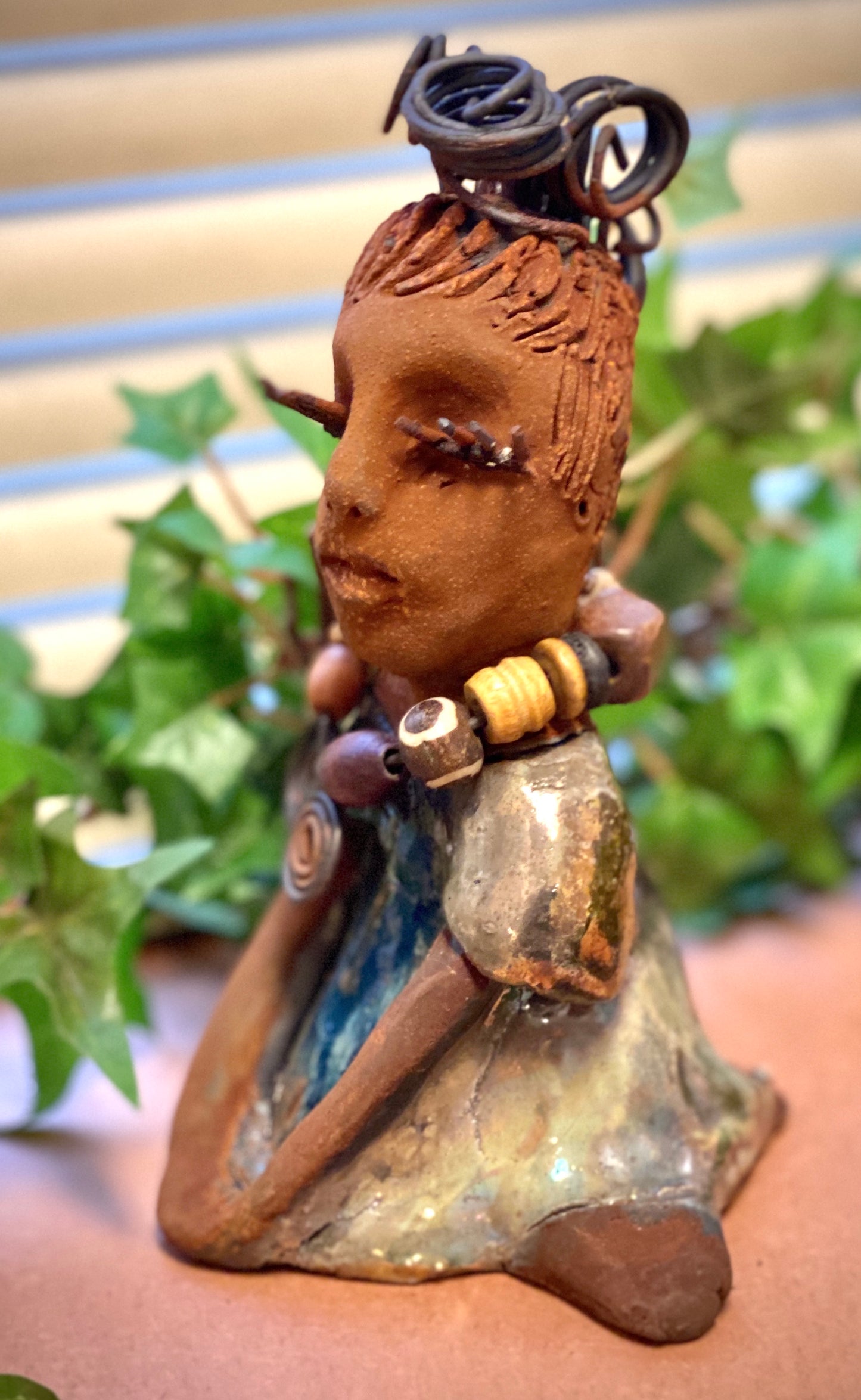 Janet stands 6" x 4" x 4" and weighs 14 ozs. Janet has a honey brown complexion with wire hair. She wears long lashes and has a alligator green metallic dress. She wears an awesome wood bead necklace. Janet has her long loving arms around her knees as she rest and waits.