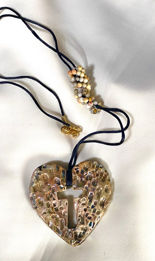 Have A Heart ! Each heart pendant is handmade with love! It is 3"x 3" and weighs approx. 3ozs. This pendant has a white and gold metallic raku glazes that renders a unique translucent  patina. The heart has a textured with cut out cross pattern . It holds a spiral of multicolored mini beads on a spiral copper wire. This pendant has a nice 12" black suede cord!
