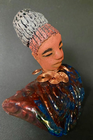 Meet Tia! Tia looks up with joy and anticipation! Tia stands 7" x 6" x 4" and weighs 1.90 lbs. She has a beautiful textured copper and blue robe. Tia has braided clay hair up in a bun. She has a honey brown complexion and soft light brown lips. Tia will make for great conversation in your home.  Free Shipping! Check out our Shipping and Return policy  