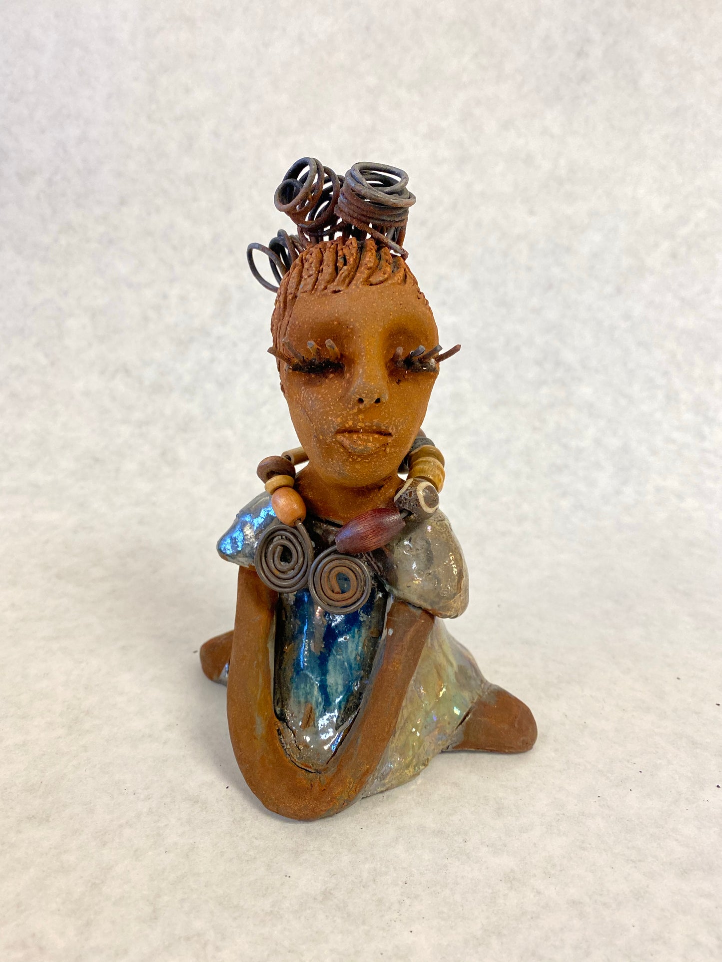 Janet stands 6" x 4" x 4" and weighs 14 ozs. Janet has a honey brown complexion with wire hair. She wears long lashes and has a alligator green metallic dress. She wears an awesome wood bead necklace. Janet has her long loving arms around her knees as she rest and waits.